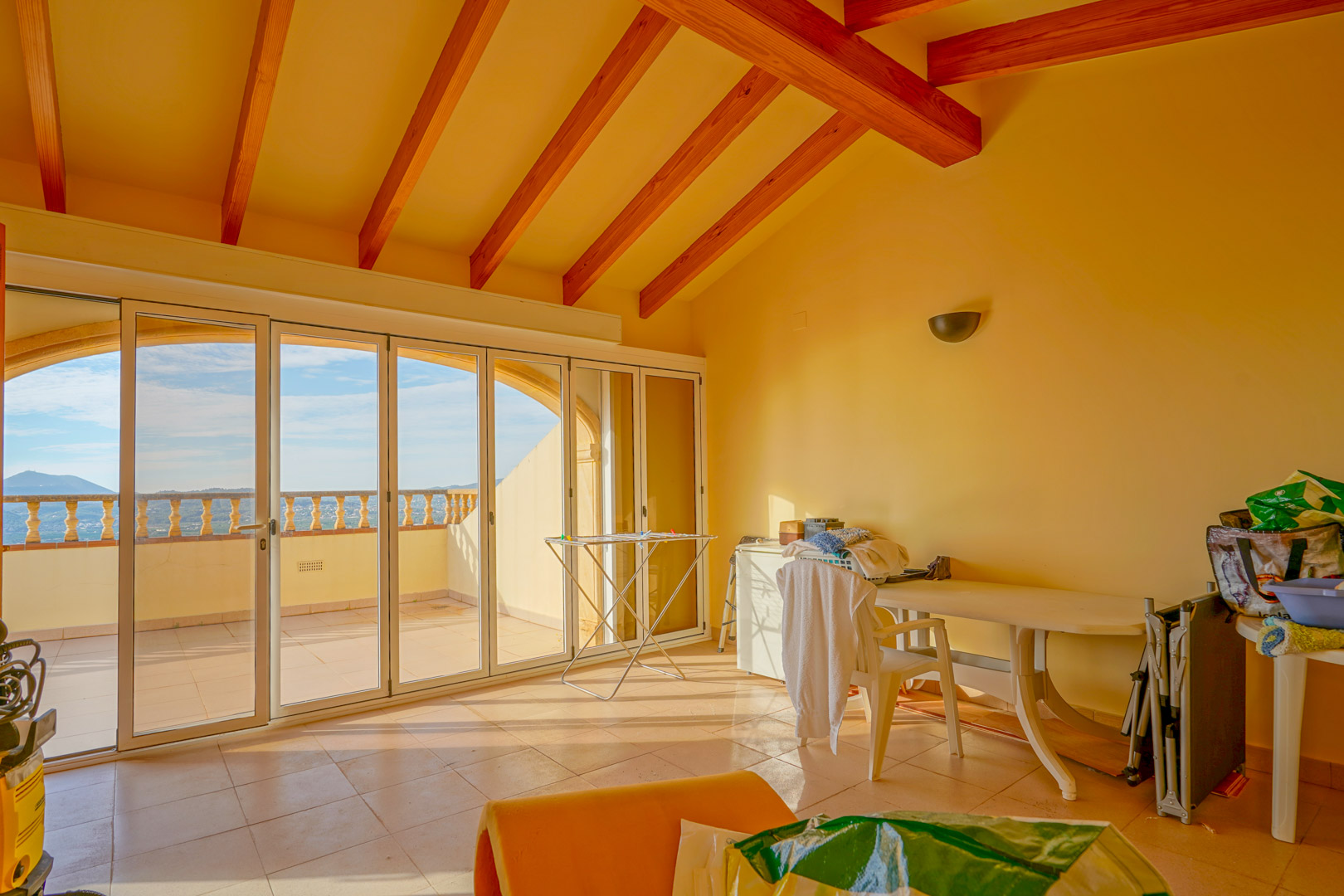 Sala en la planta superior con techos altos de vigas de madera y amplios ventanales que conectan con una terraza exterior con vistas despejadas a la montaña.