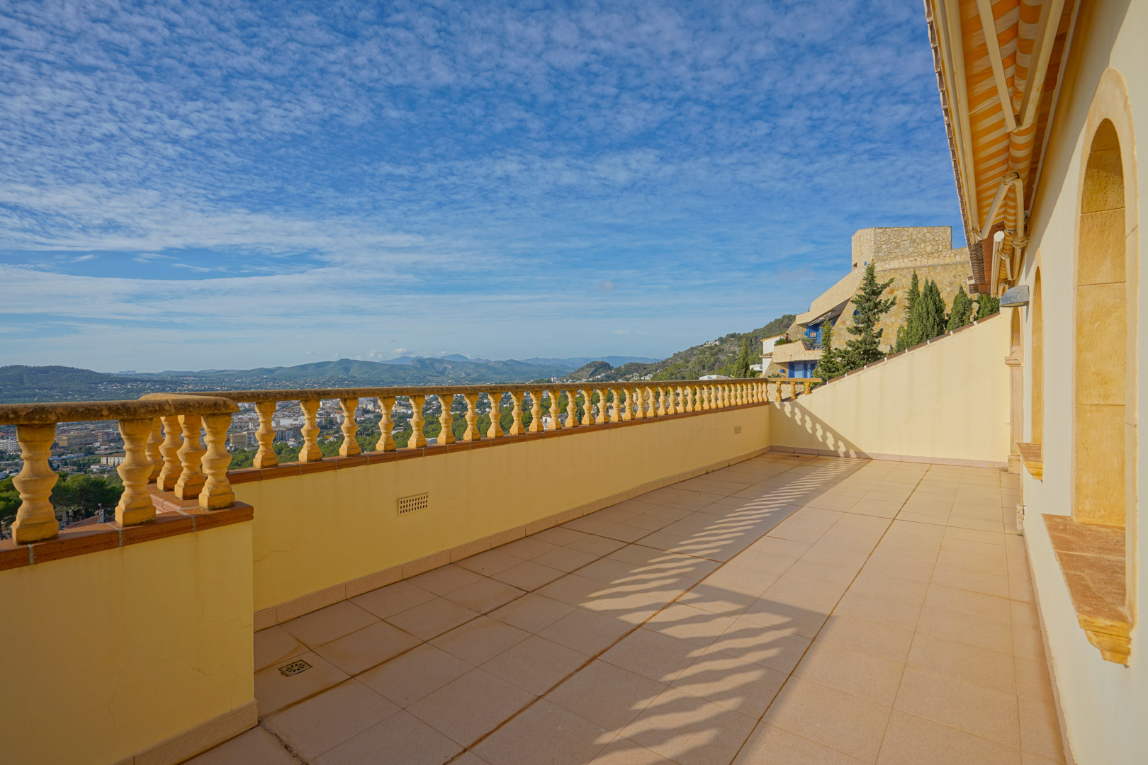 Terraza superior con balaustrada tradicional y suelos cerámicos, ofreciendo vistas panorámicas hacia el valle de Jávea y las montañas circundantes bajo un cielo despejado.