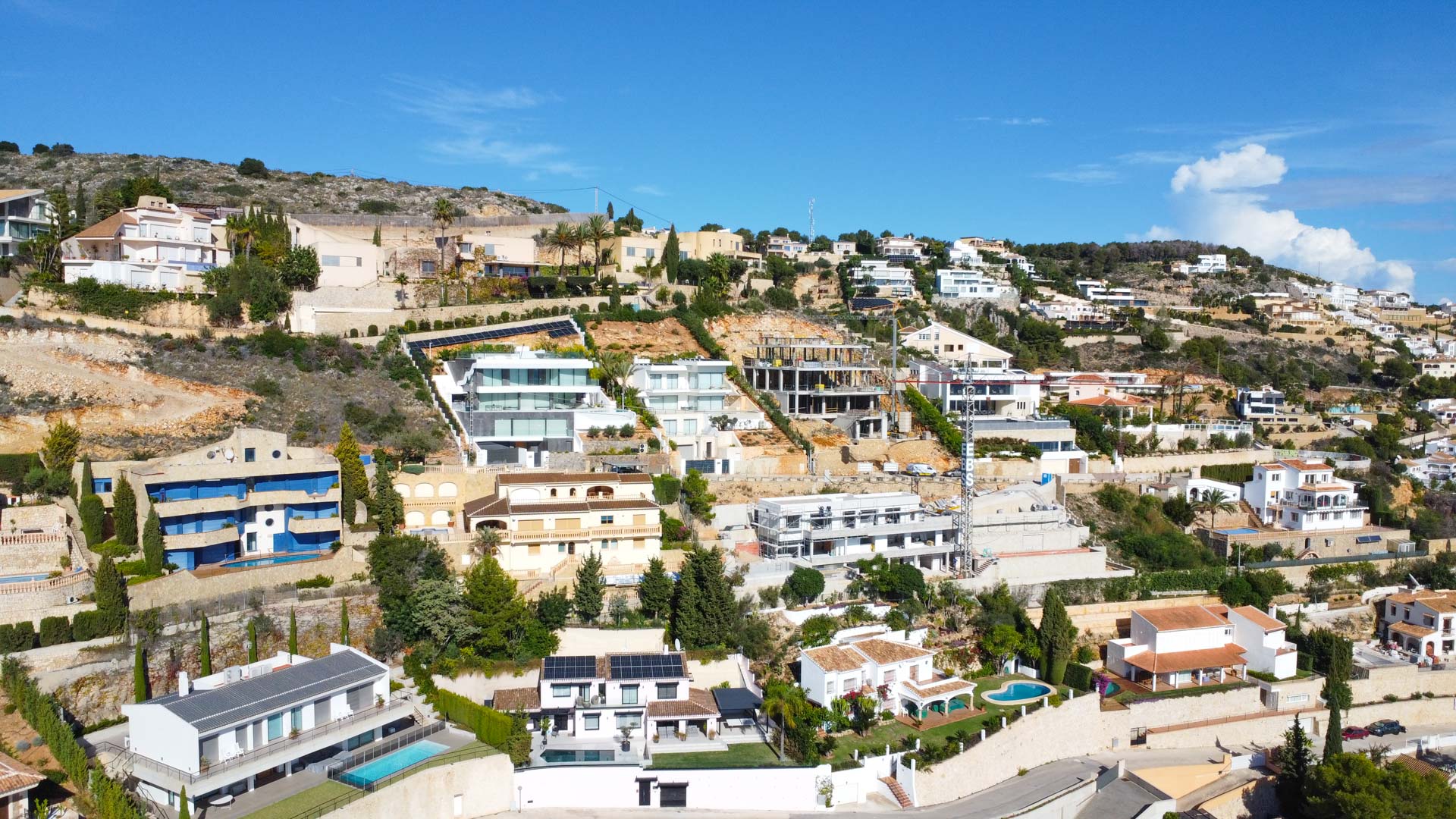 Vista aérea de la urbanización La Corona en Jávea, mostrando la disposición escalonada de las villas en la ladera y la arquitectura mediterránea predominante.