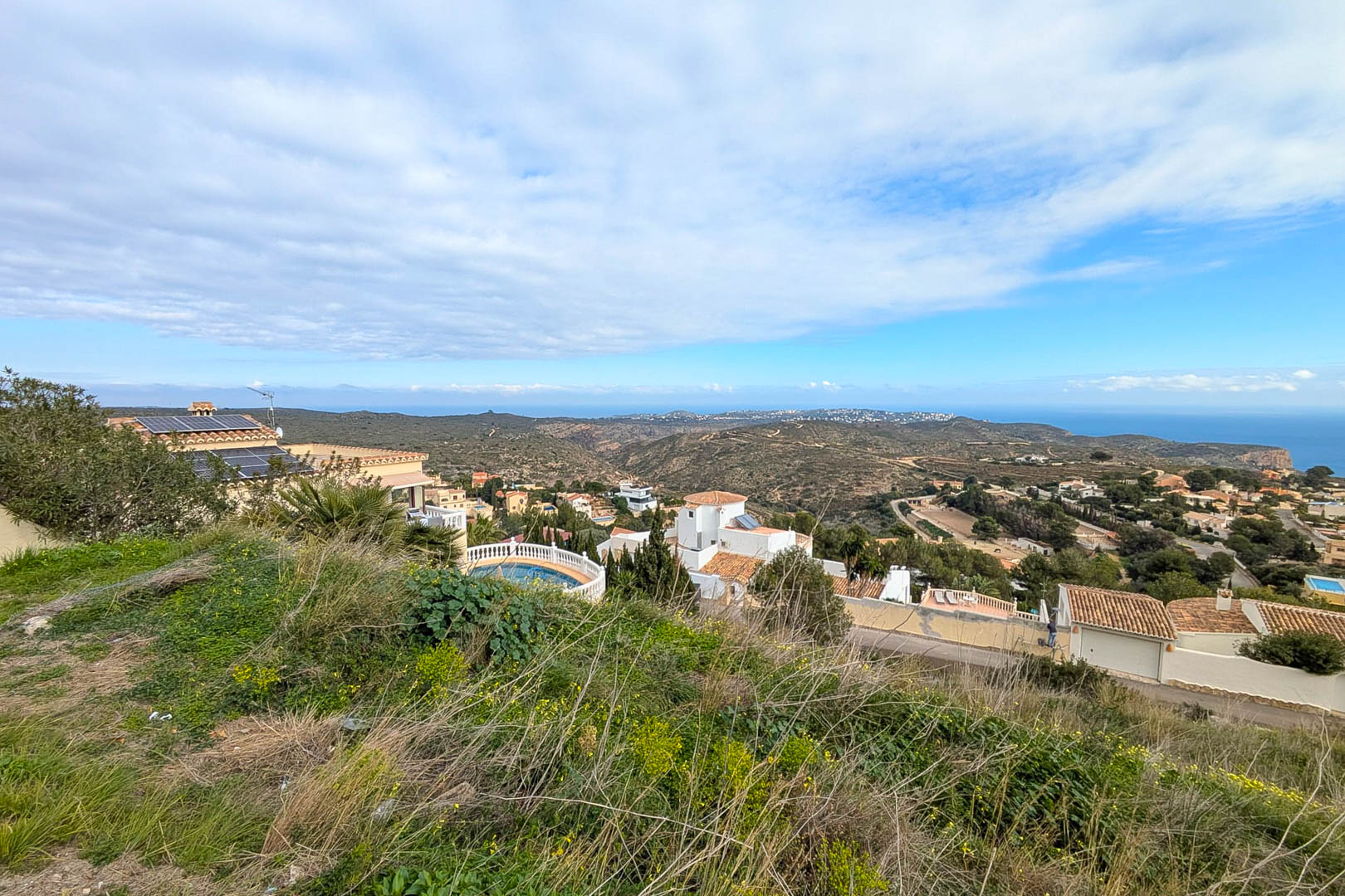 Vistas panorámicas desde la parcela elevada hacia el mar Mediterráneo y el valle, rodeada de vegetación natural y villas residenciales en Cumbre del Sol.