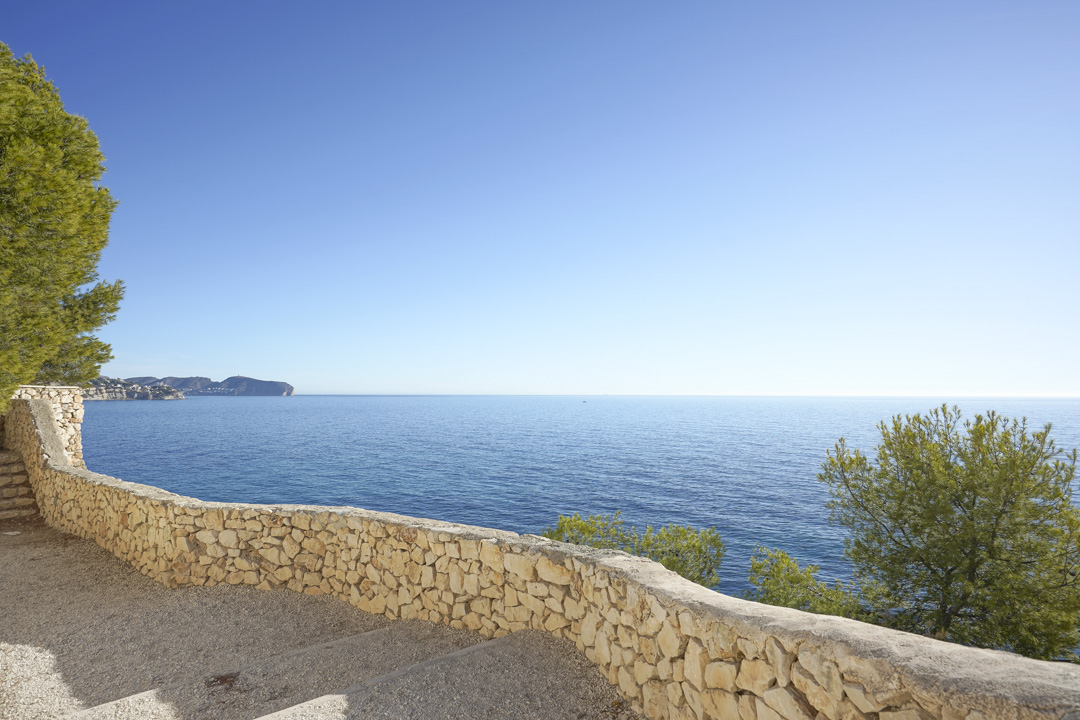 Vista panorámica al mar Mediterráneo desde una terraza con muro de piedra natural. El entorno incluye pinos autóctonos y una perspectiva despejada de la costa de Calpe.