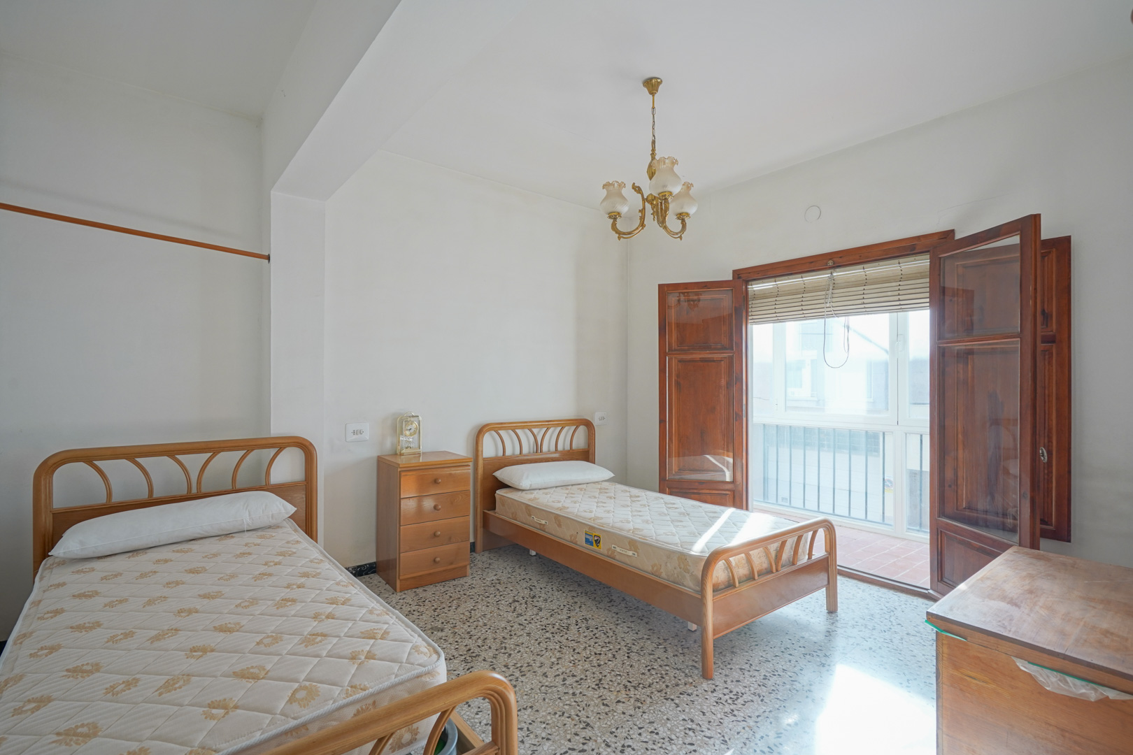 Dormitorio con dos camas individuales, suelos de terrazo y acceso directo a una terraza a través de puertas de madera natural.