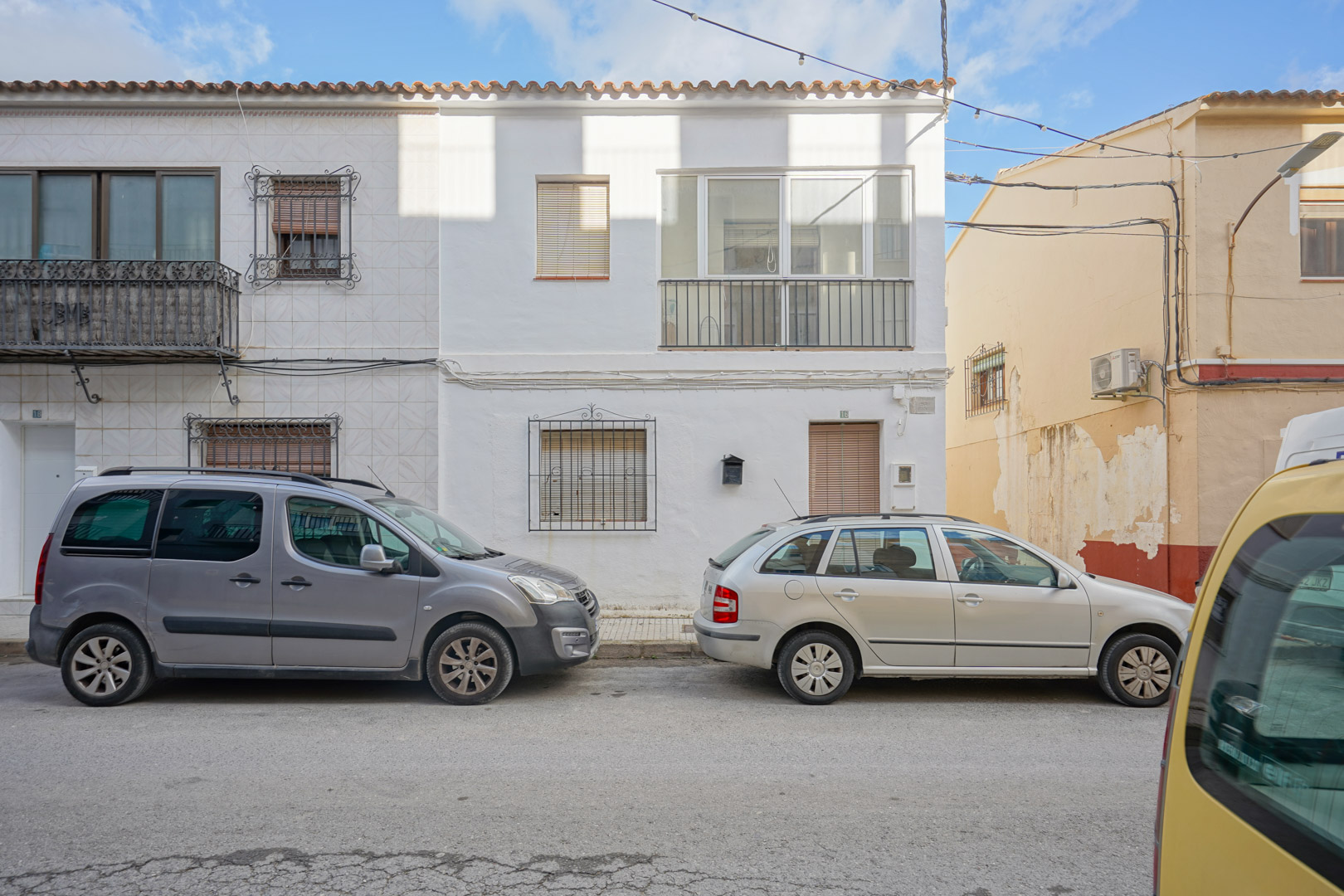 Fachada exterior de la casa adosada en Benissa con paredes blancas, rejas de hierro forjado en planta baja y una terraza acristalada en el nivel superior.