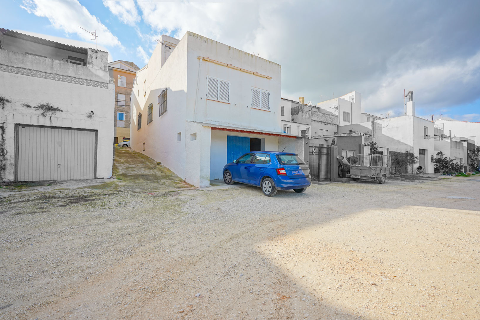 Fachada exterior de la vivienda en Benissa con acceso al garaje en el semisótano, rampa lateral y ventanas con contraventanas blancas.