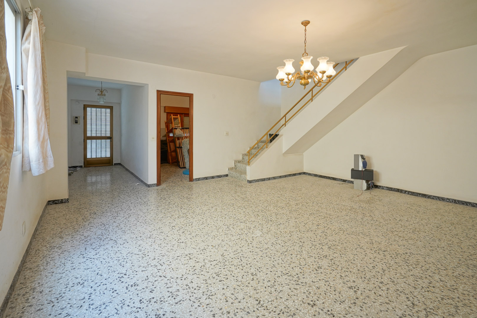 Salón principal con suelos de terrazo, escalera de obra con barandilla metálica y acceso al vestíbulo y dormitorios de la planta baja.