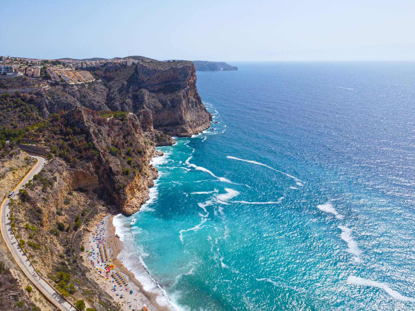 Vista aérea de la Cala del Moraig en Cumbre del Sol, destacando sus acantilados escarpados, aguas turquesas y el acceso serpenteante hacia la playa.