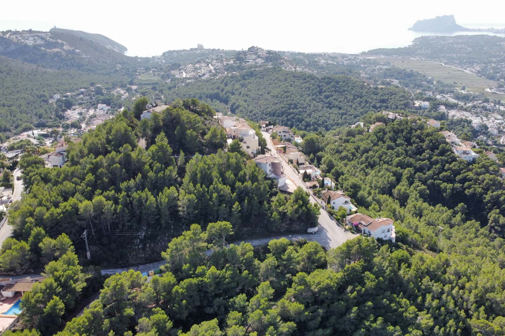 Vista aérea de la zona residencial en Paichi, Moraira, destacando su elevación sobre colinas arboladas con vistas panorámicas al mar y al Peñón de Ifach.