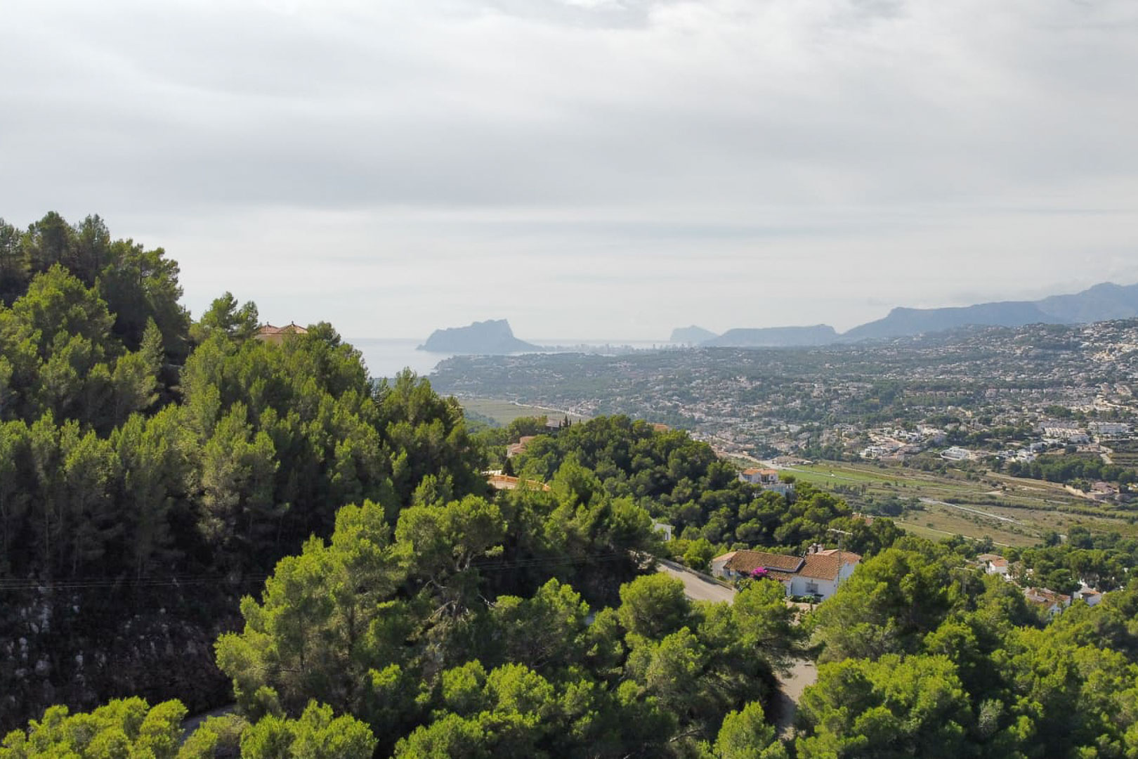 Vista panorámica elevada desde la parcela en Paichi, destacando el denso pinar, el valle residencial y la silueta del Peñón de Ifach en el horizonte marino.