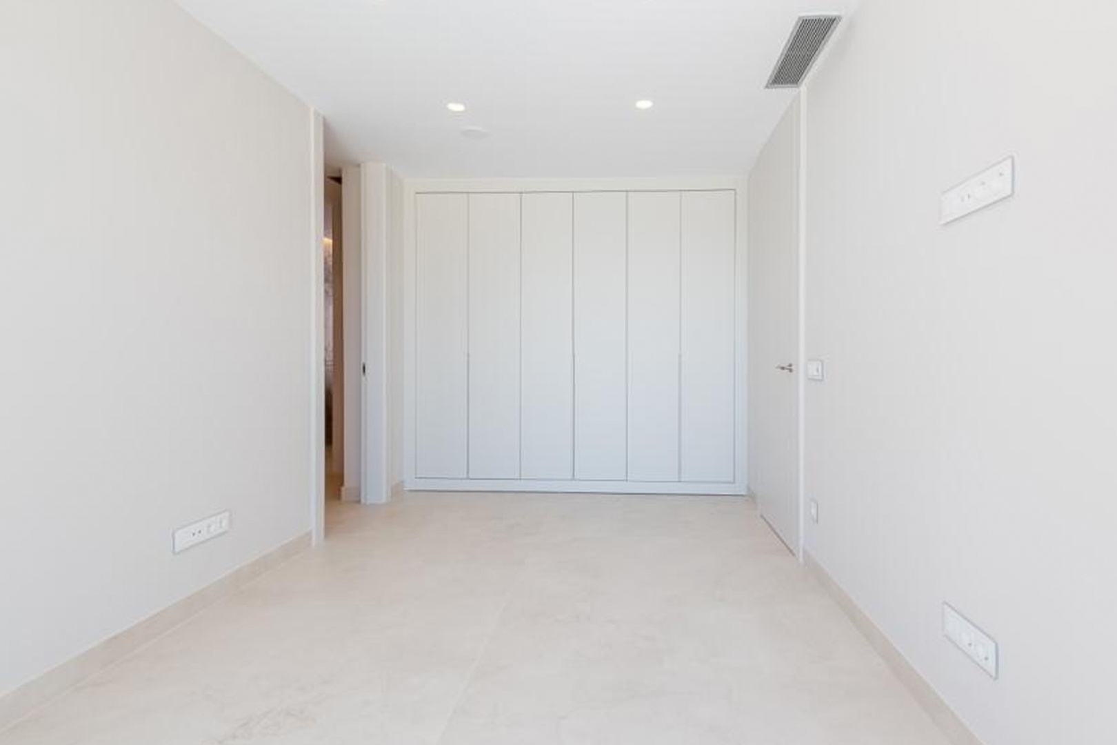 Dormitorio minimalista con armarios empotrados de suelo a techo, suelos de gres porcelánico claro y sistema de climatización por conductos integrado en el techo.