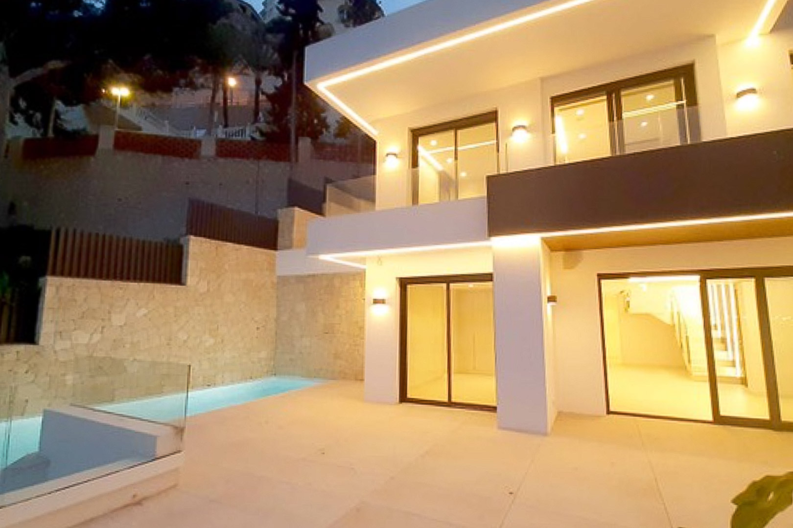 Fachada moderna con iluminación LED integrada, terraza de gres porcelánico y piscina privada junto a muros de piedra natural.