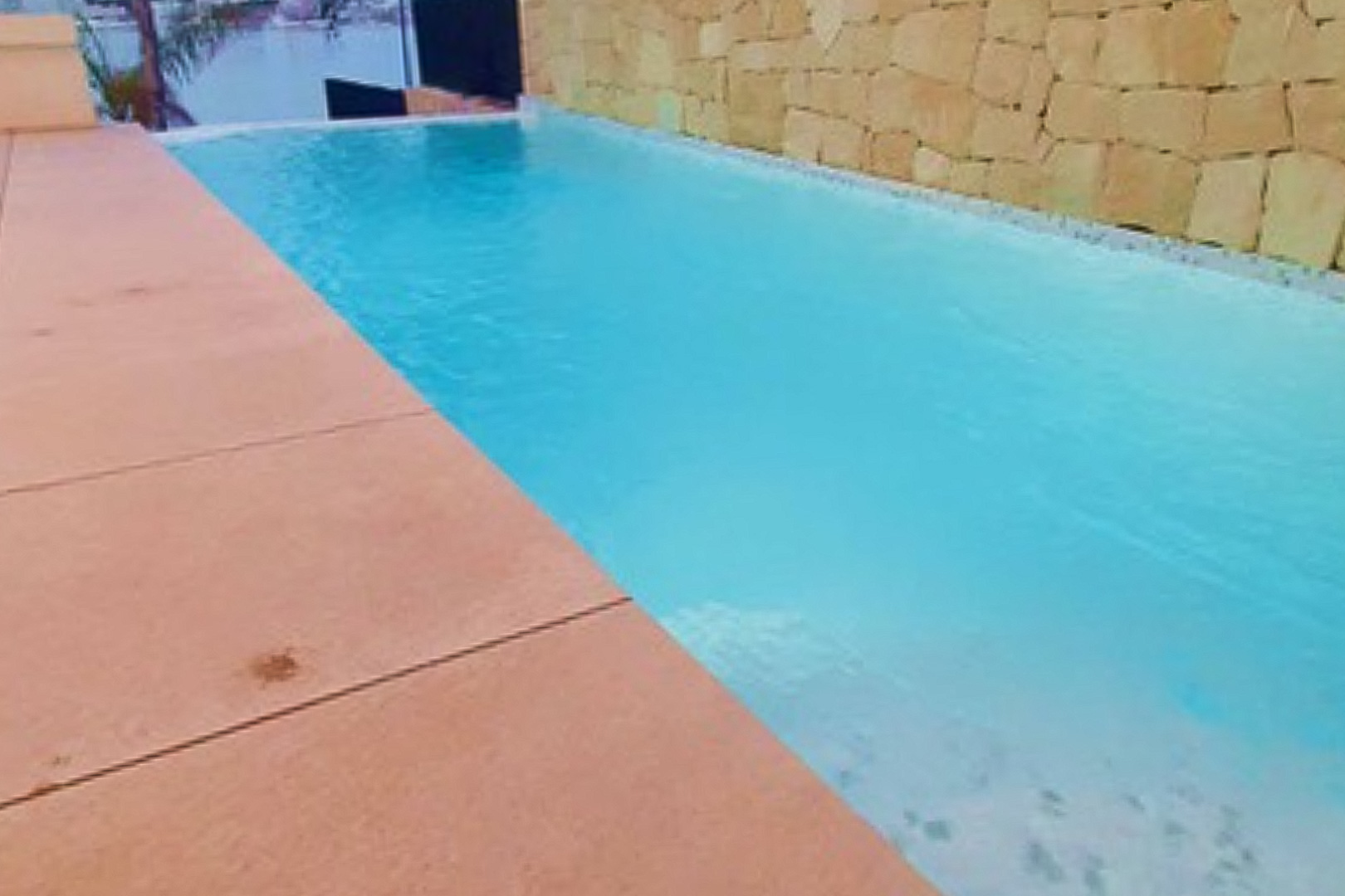 Piscina privada de borde infinito con vistas al mar, integrada en una terraza con suelo cerámico y un muro decorativo de piedra natural.