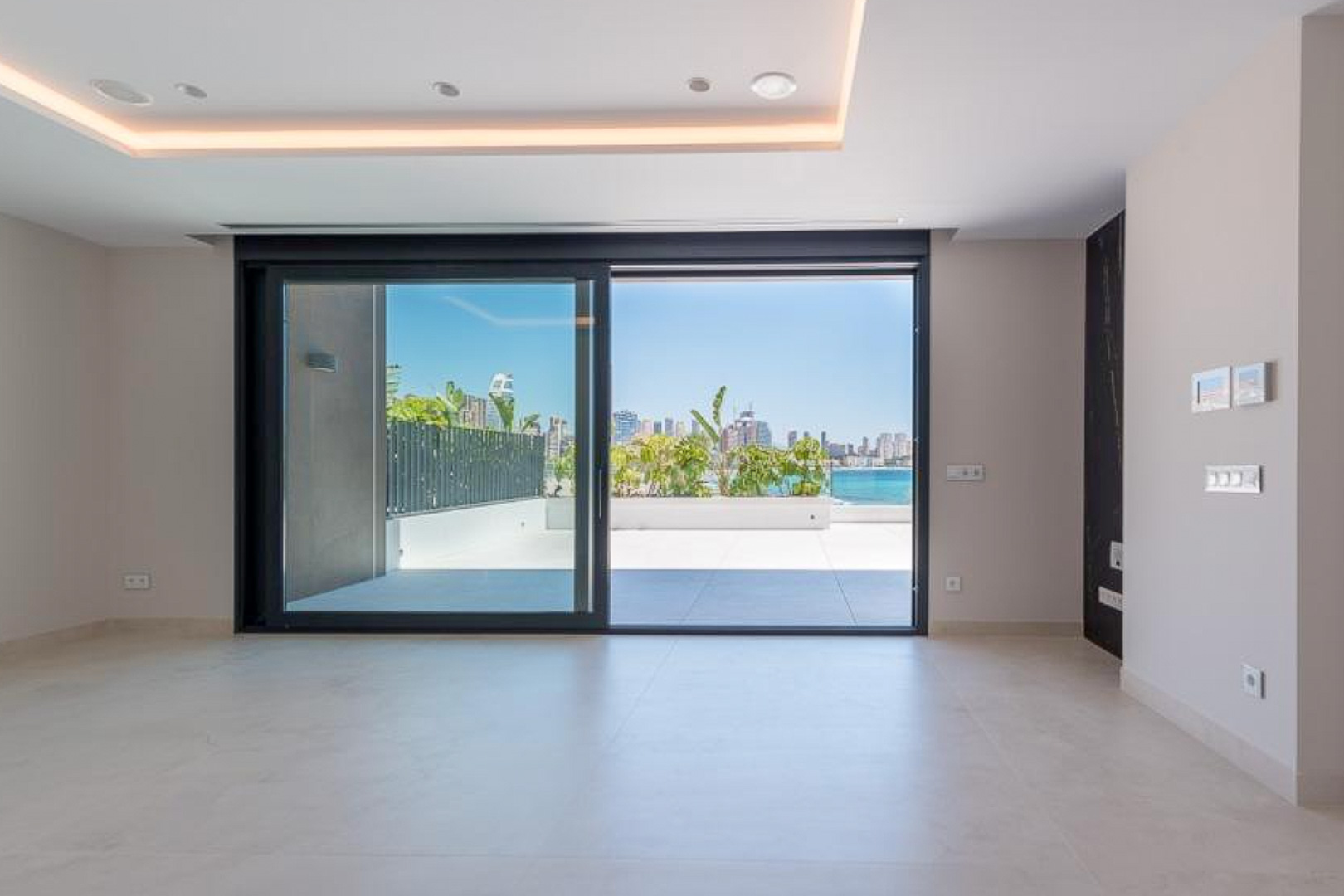 Salón luminoso con suelos cerámicos de gran formato y ventanales correderos que acceden a una terraza privada con vistas al mar y al skyline de Benidorm.