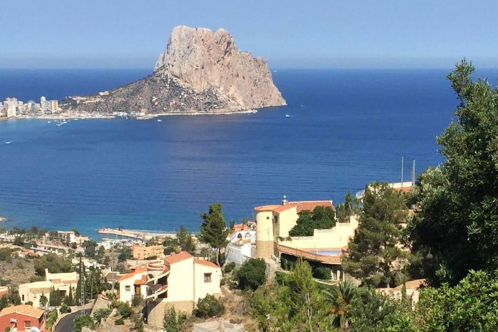 Vista panorámica elevada hacia el Peñón de Ifach y el mar Mediterráneo, capturando el entorno residencial de Calpe rodeado de vegetación autóctona.