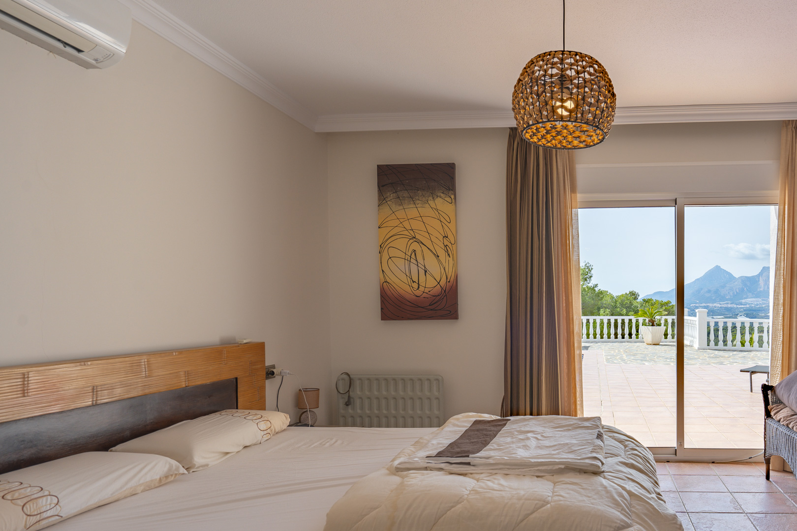 Dormitorio con cabecero de madera y aire acondicionado, con acceso directo a la terraza y vistas panorámicas a las montañas de Altea.