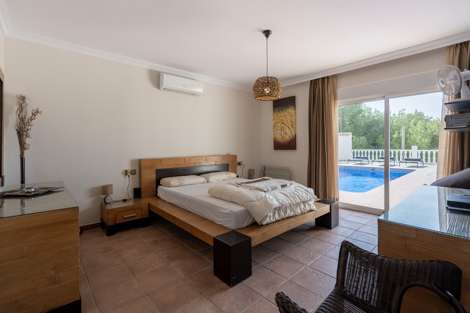 Dormitorio principal con suelo de terracota, aire acondicionado y acceso directo a la terraza de la piscina a través de amplios ventanales correderos.