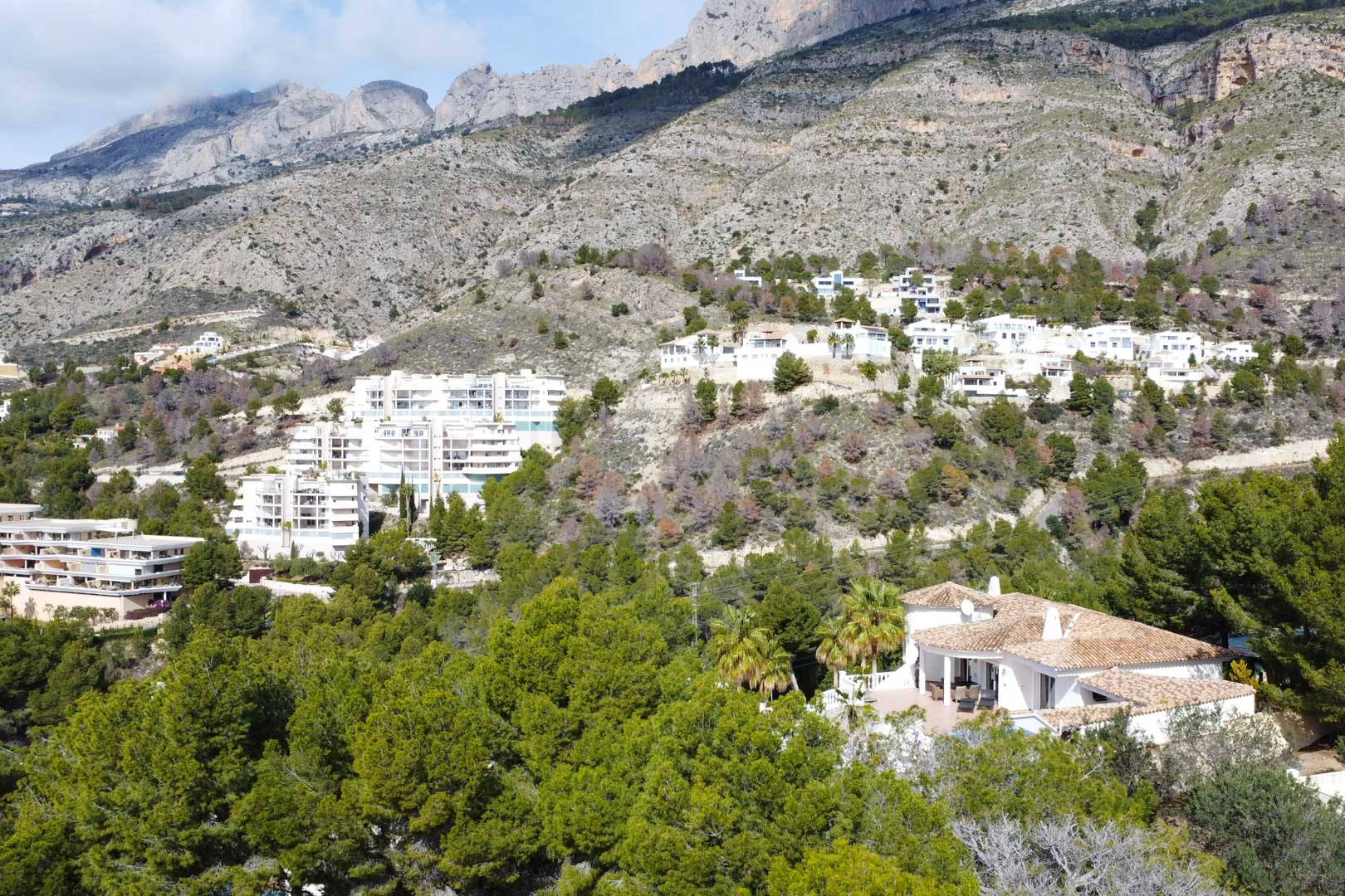 Vista aérea de la villa mediterránea con tejado de teja, rodeada de pinos y situada a los pies de la imponente Sierra de Bernia en Altea.