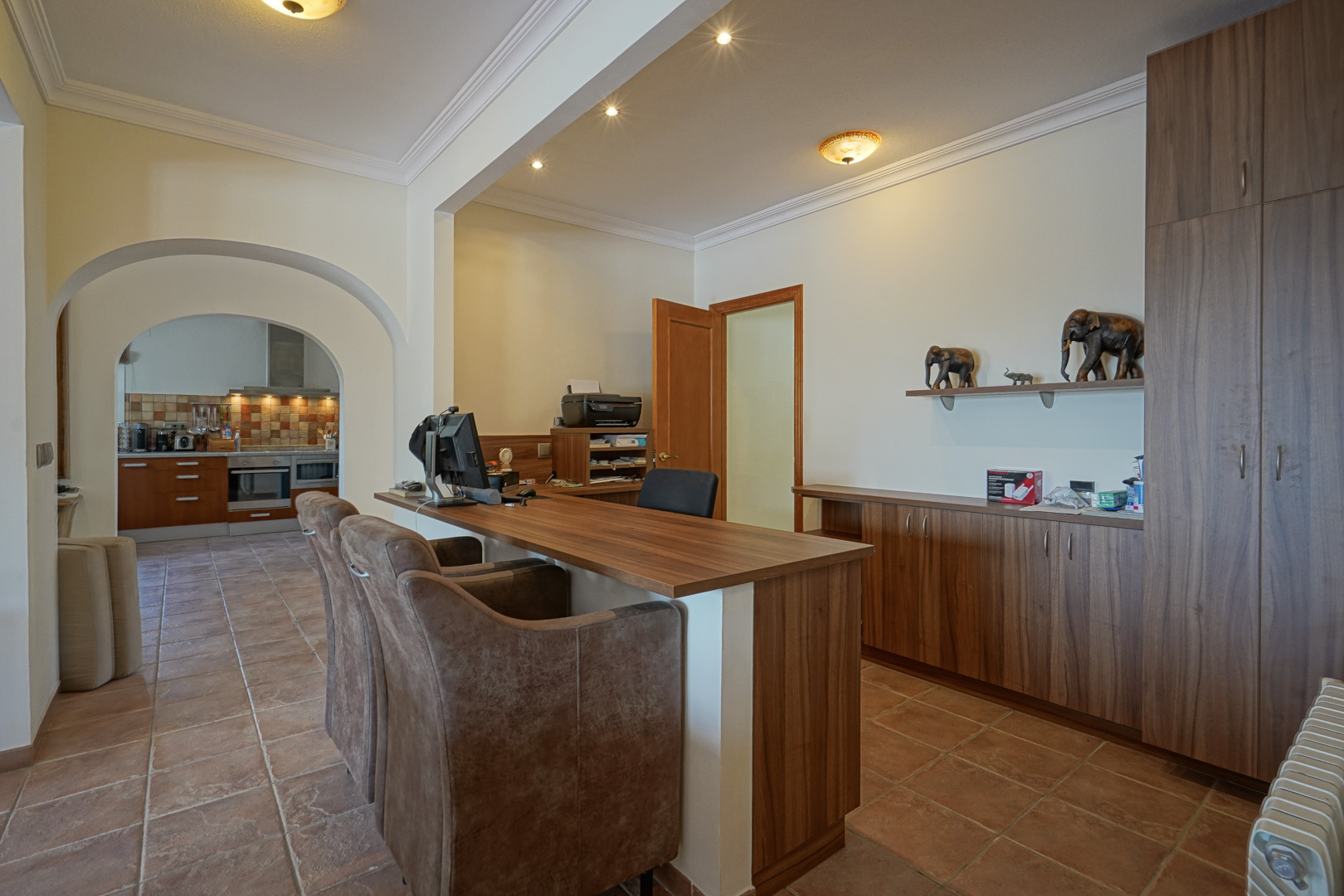 Zona de despacho con mobiliario de madera a medida, suelos de terracota y arcos decorativos que conectan visualmente con la cocina.