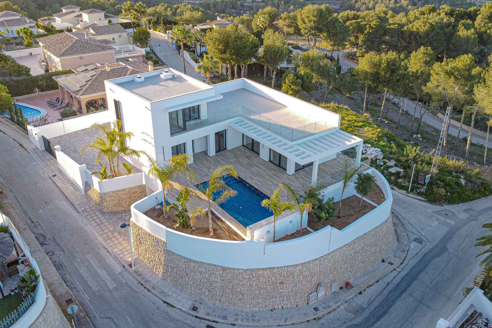 Vista aérea de la villa moderna con piscina azul, terraza con pérgola y jardín mediterráneo en Benimeit, Moraira.