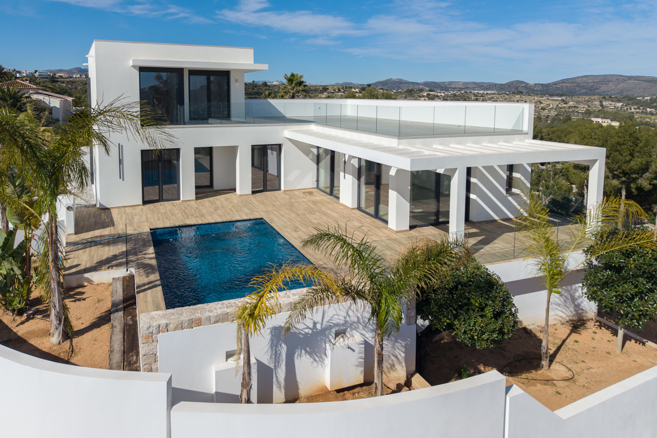 Vista aérea de la villa moderna con piscina azul, terraza de madera y barandilla de cristal en Benimeit, Moraira.