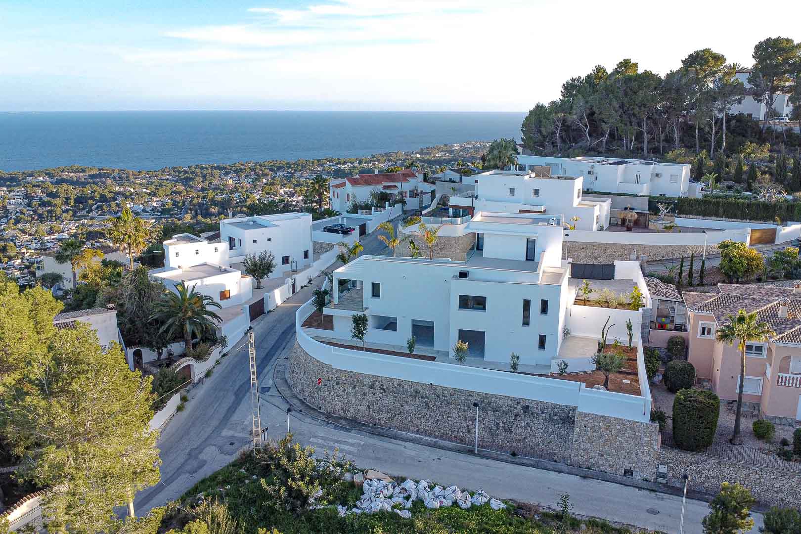 Vista aérea de villa moderna blanca con muros de piedra y vistas al mar en Benimeit, Moraira.