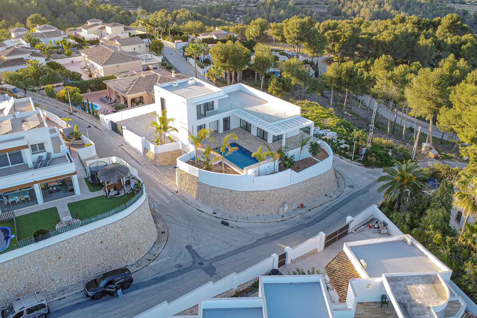 Vista aérea de villa moderna con piscina azul, rodeada de muro de piedra y vegetación en Benimeit, Moraira.