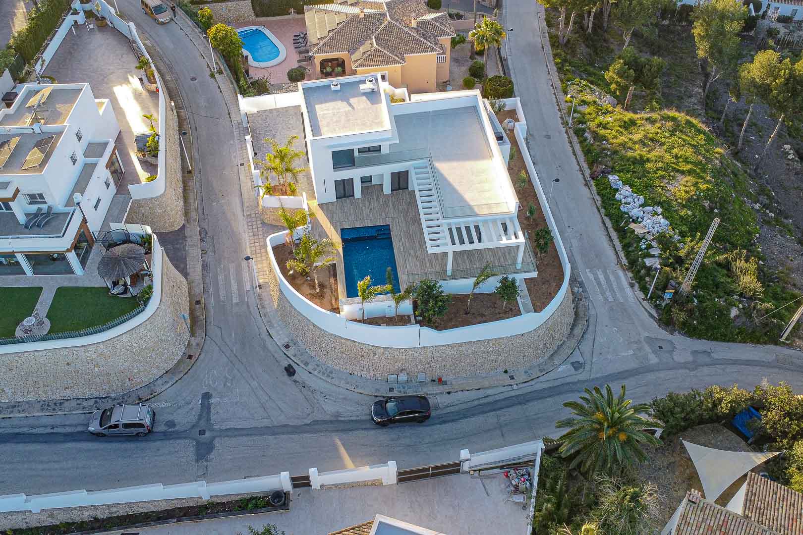 Vista aérea de villa moderna con piscina azul, terrazas de madera y jardín mediterráneo en Benimeit, Moraira.