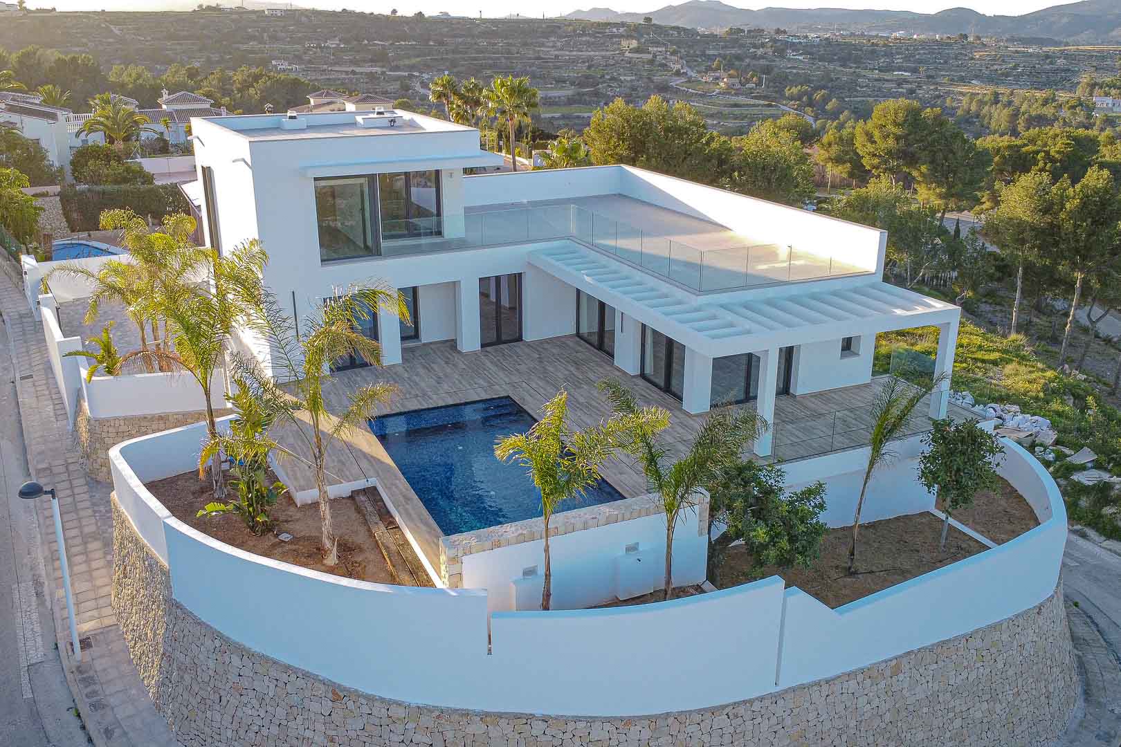 Vista aérea de villa moderna con piscina azul y muros blancos con detalles de piedra en Benimeit, Moraira.