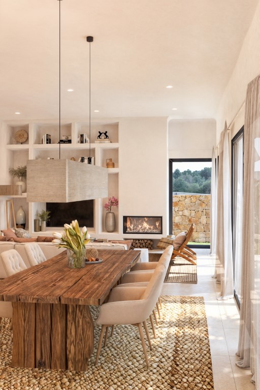 Comedor luminoso con mesa rústica de madera, alfombra de fibra natural y estanterías empotradas en la pared.