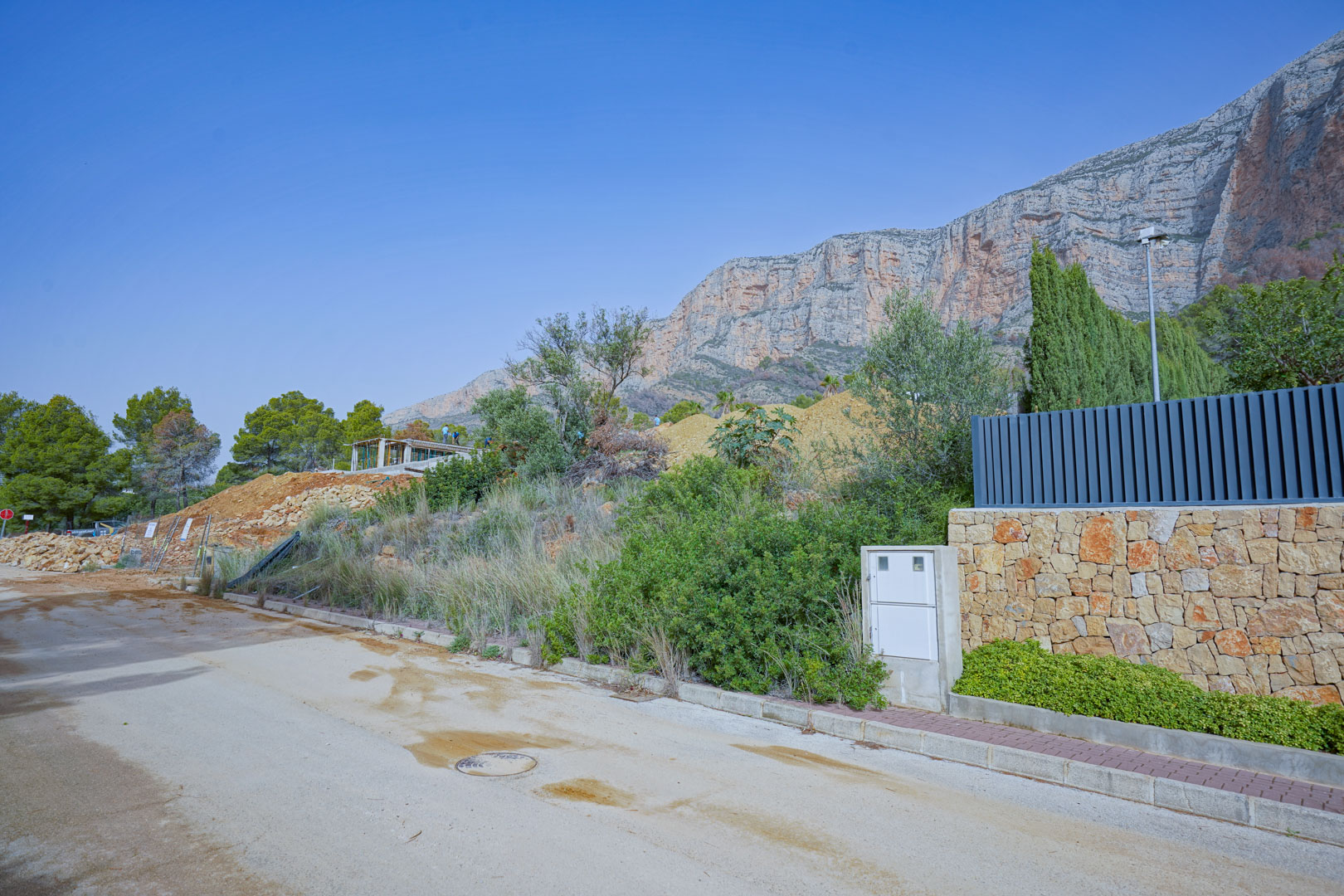 Parcela en fase de construcción inicial bajo los acantilados del Montgó, con la estructura principal visible y muro perimetral de piedra natural.