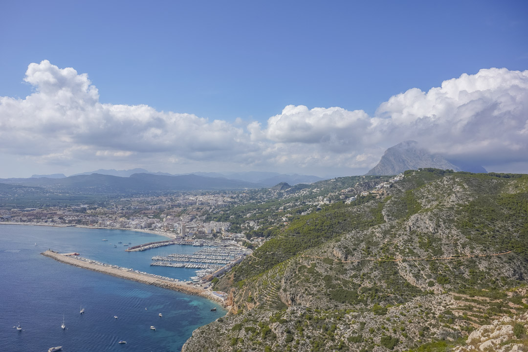 Vista aérea del puerto de Jávea y la costa mediterránea, destacando el relieve montañoso y el icónico macizo del Montgó al fondo.