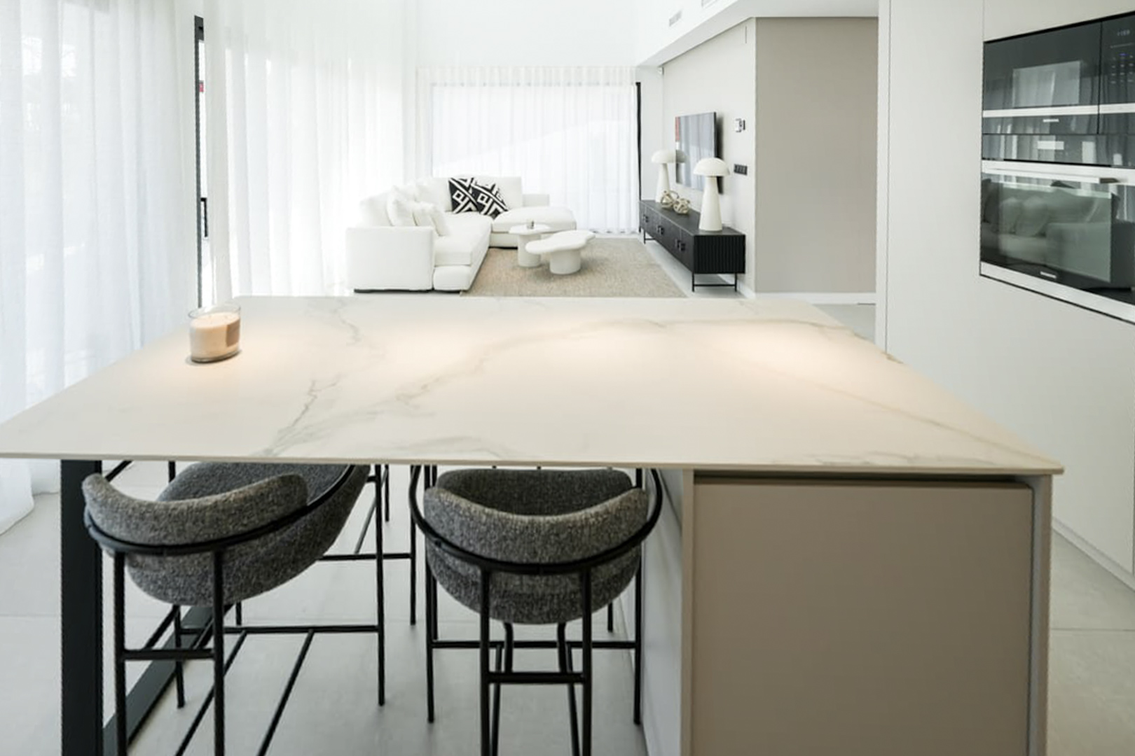 Detalle de la isla de cocina con encimera de mármol y taburetes tapizados en gris.