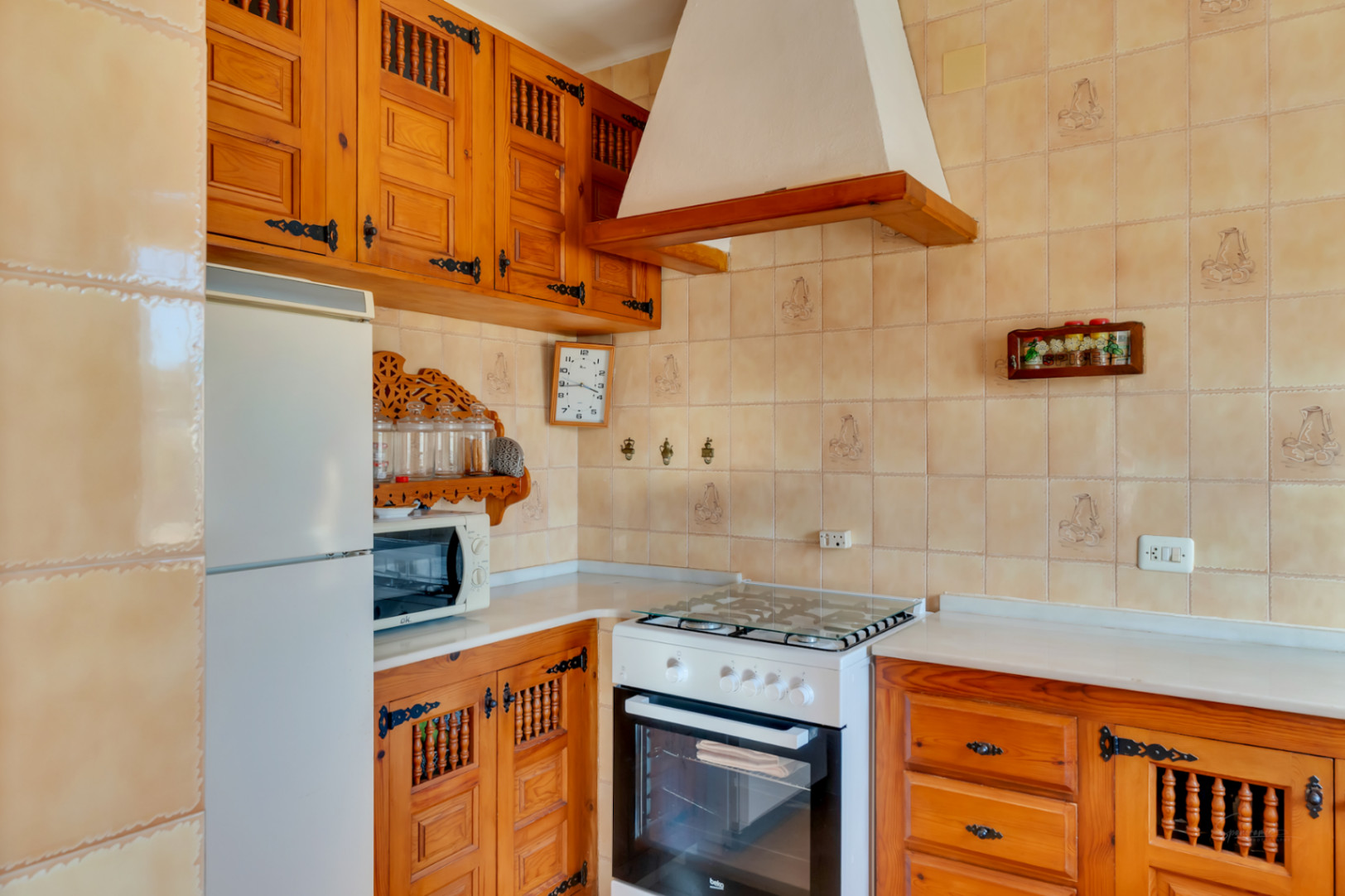 Cocina de estilo tradicional con armarios de madera tallada, herrajes de hierro forjado y paredes alicatadas en tonos beige con motivos decorativos.