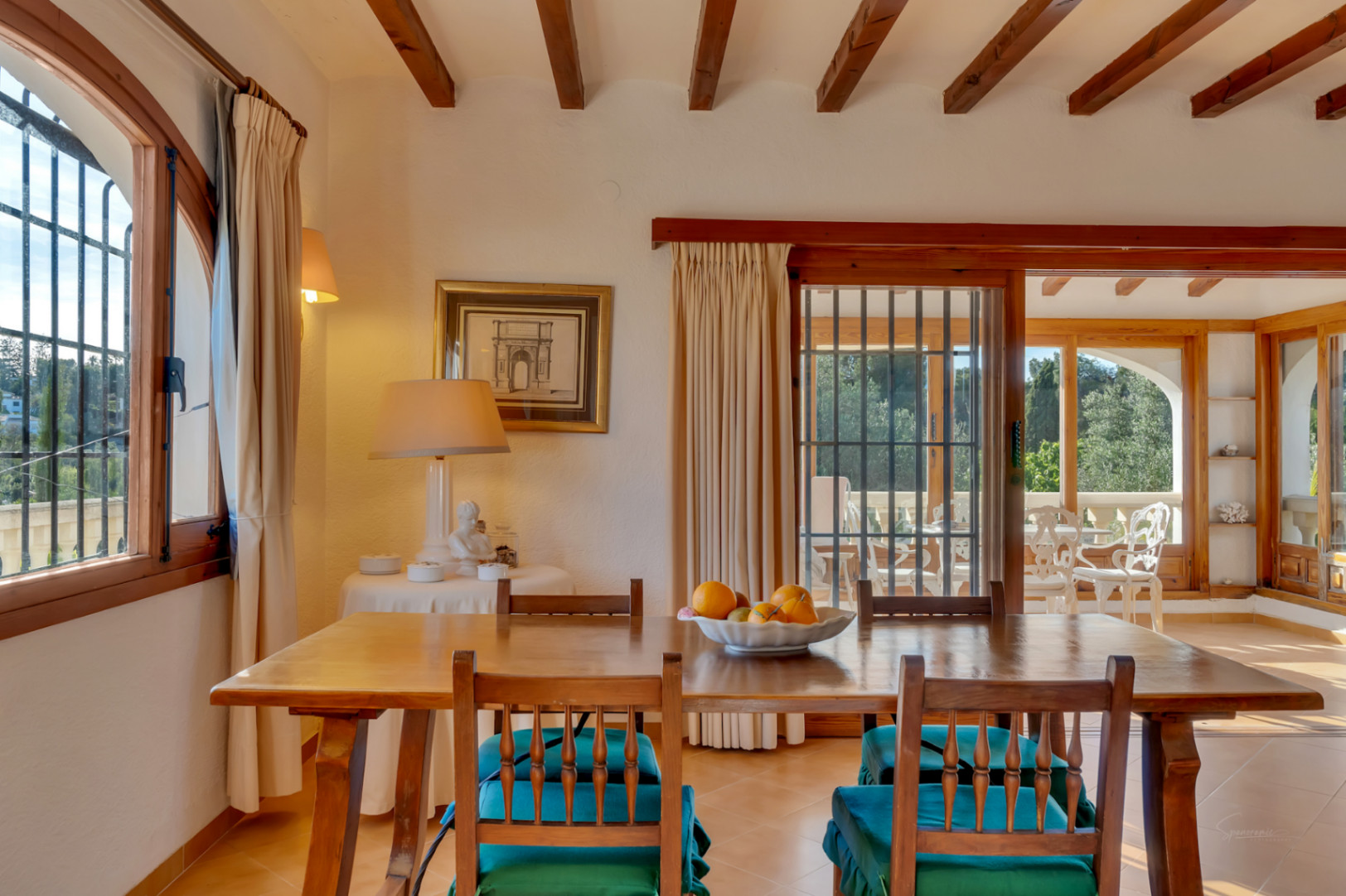 Comedor con vigas de madera vista, mobiliario rústico y acceso a la terraza acristalada mediante ventanales de madera que aportan luz natural.