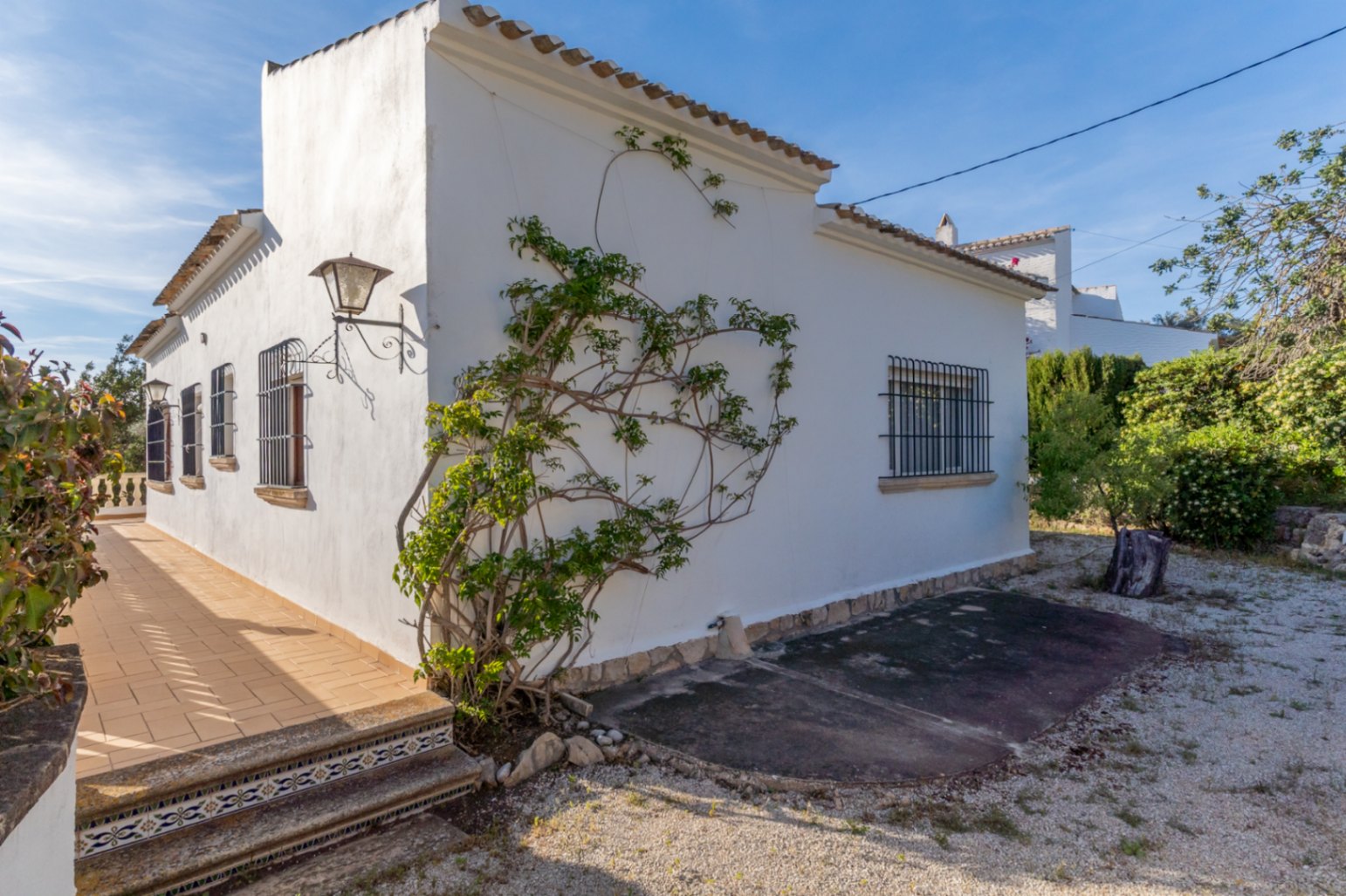 Fachada exterior de la villa con paredes blancas, ventanas con rejas de hierro forjado y una terraza lateral con escalones decorados con azulejos tradicionales.
