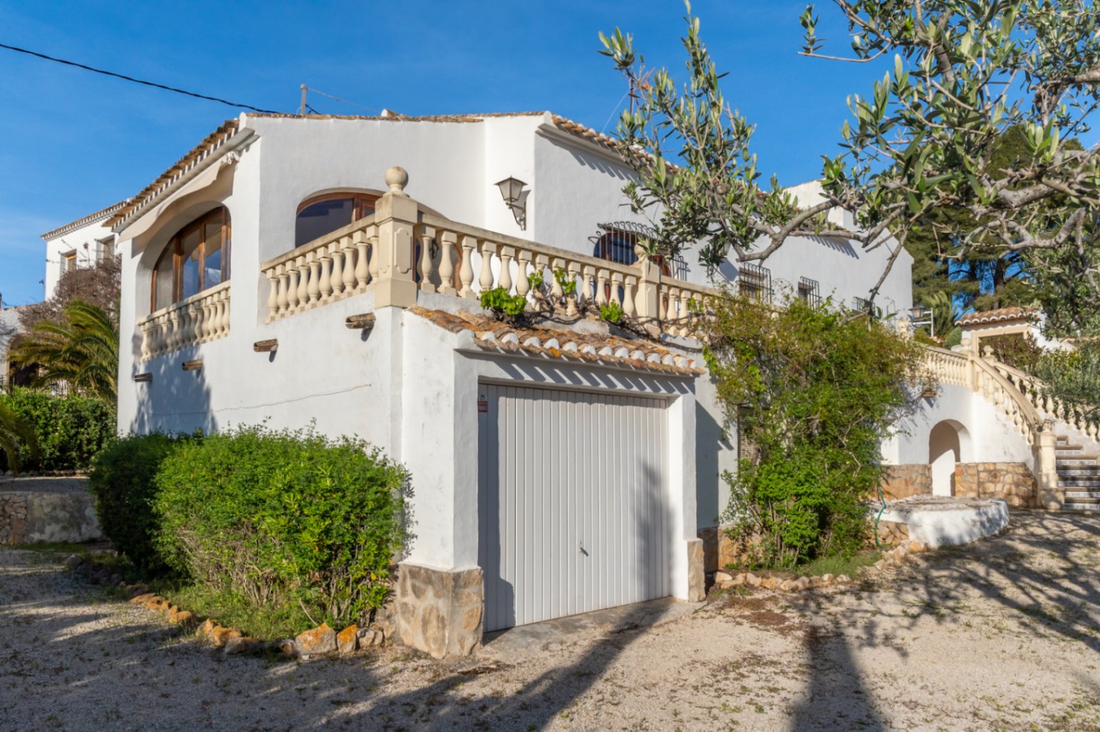 Fachada mediterránea con garaje privado, terraza superior con balaustrada de piedra y detalles arquitectónicos tradicionales en la zona de Cap Martí, Jávea.
