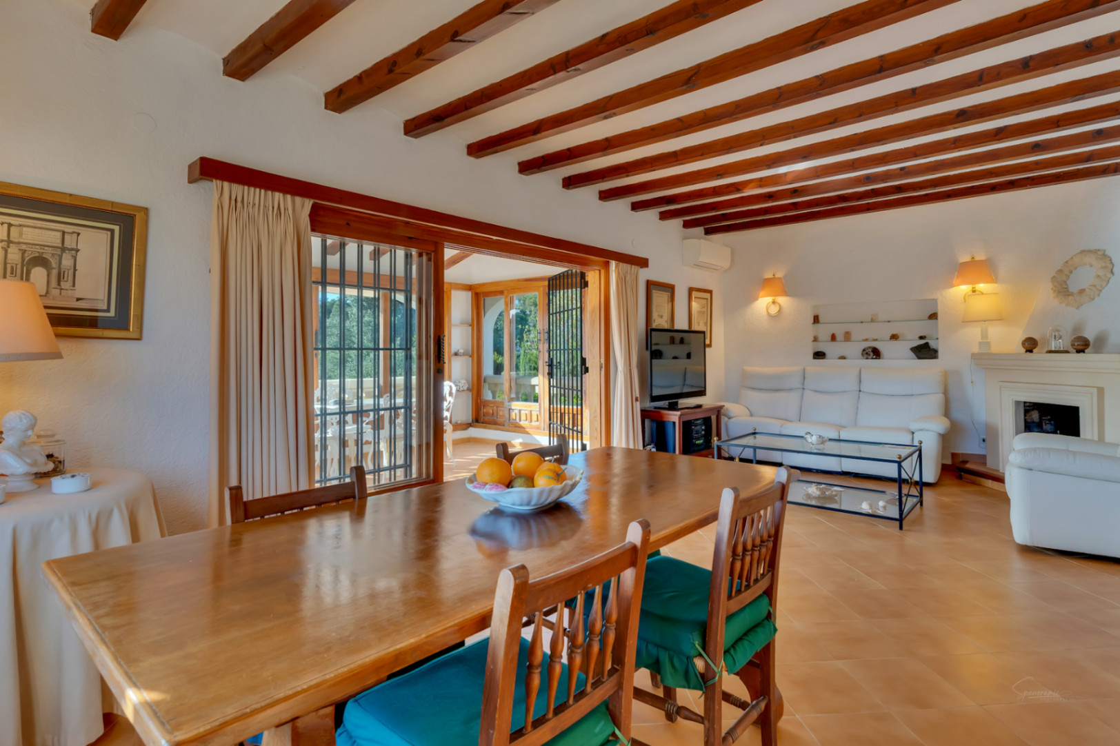 Salón-comedor de estilo mediterráneo con vigas de madera vista, suelos de terracota y acceso directo a una luminosa naya acristalada.