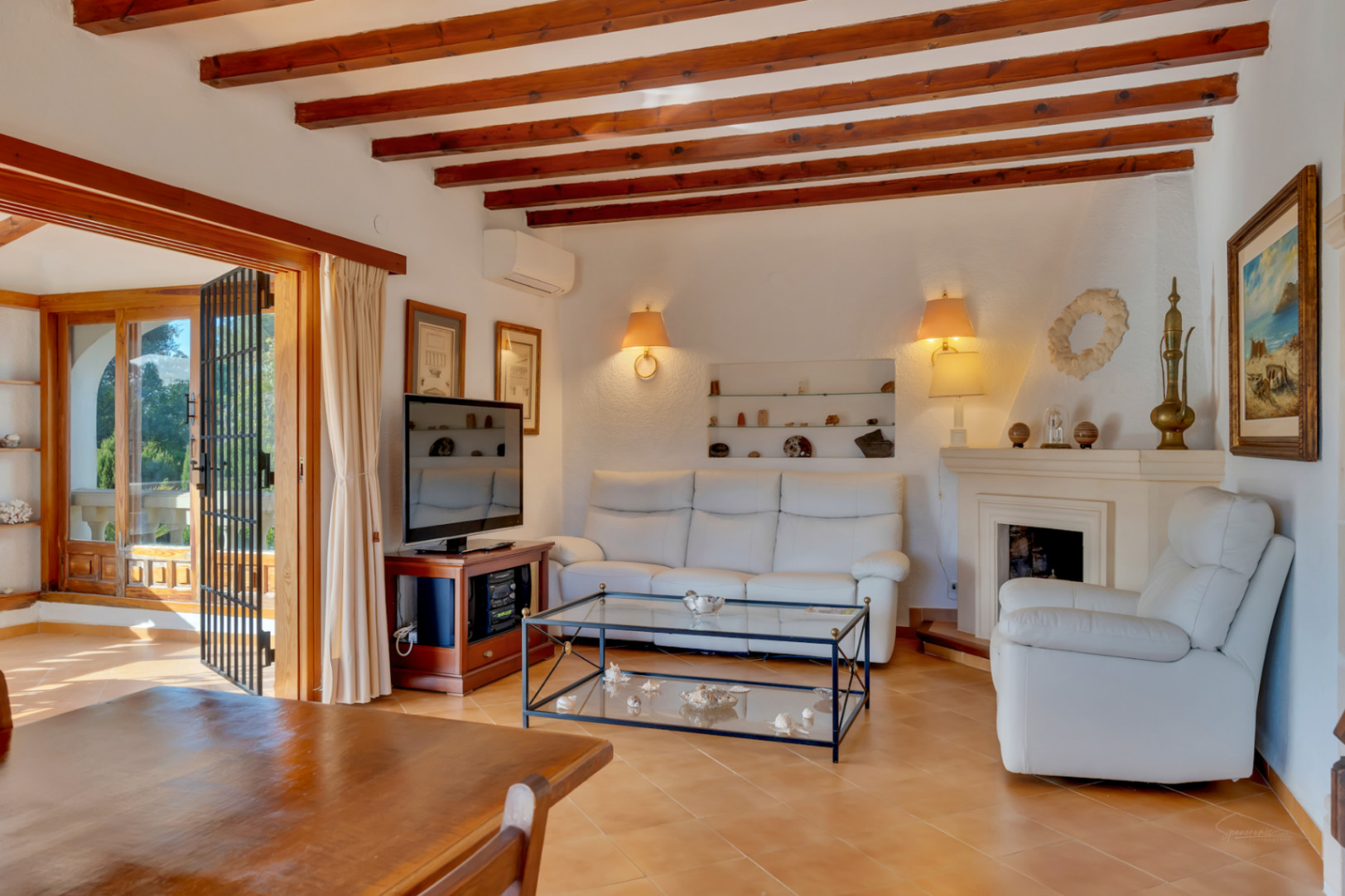Salón con vigas de madera a la vista, chimenea clásica y acceso directo a la terraza. Presenta suelos de gres y una distribución abierta hacia la zona de comedor.