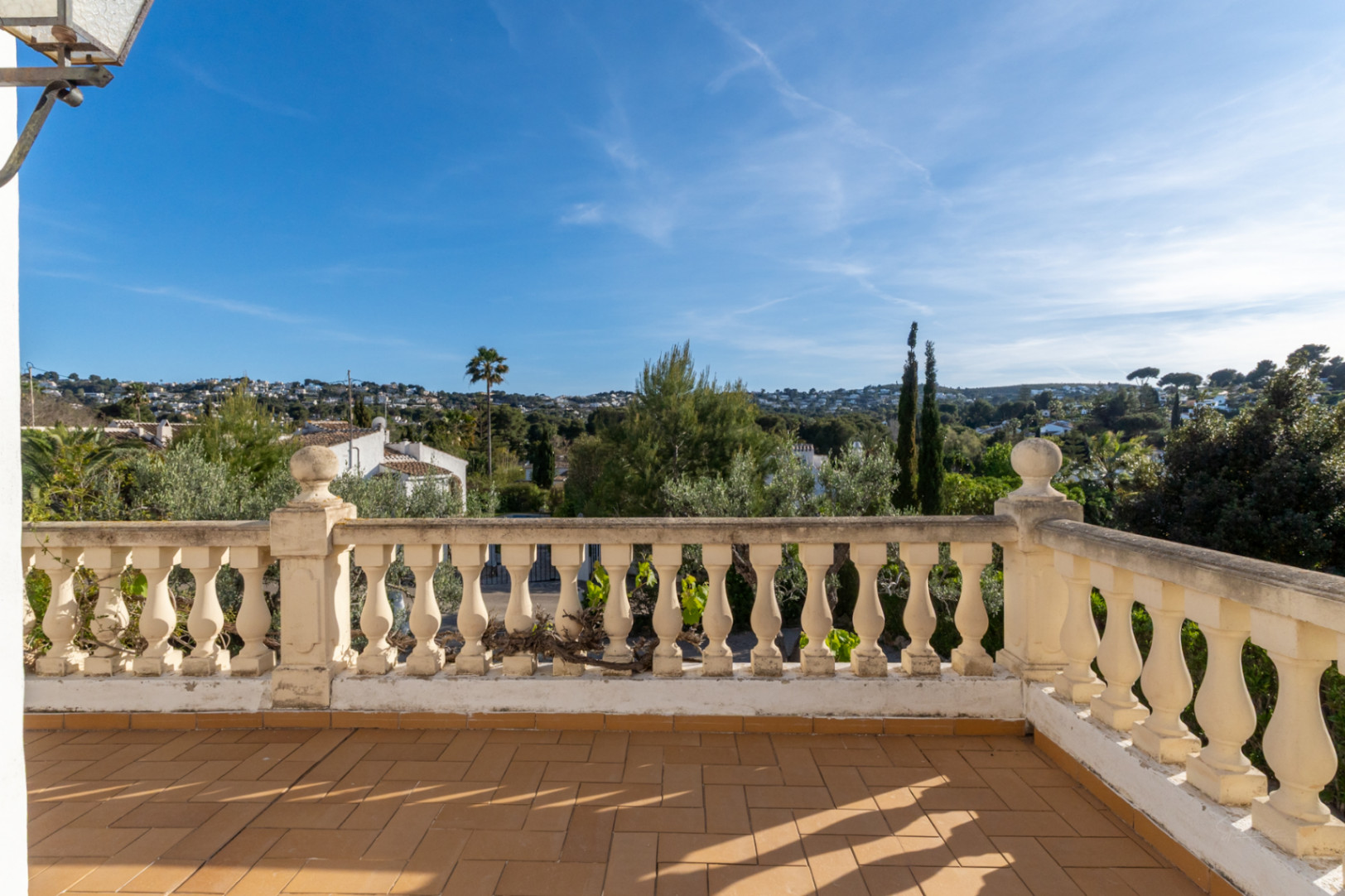 Terraza elevada con suelo de baldosas de terracota y balaustrada clásica de piedra, ofreciendo vistas despejadas al entorno residencial y la vegetación de Jávea.