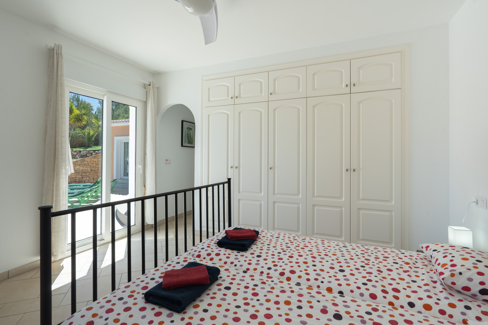 Dormitorio luminoso con armarios empotrados blancos, ventilador de techo y acceso directo a la terraza mediante puertas correderas de PVC.