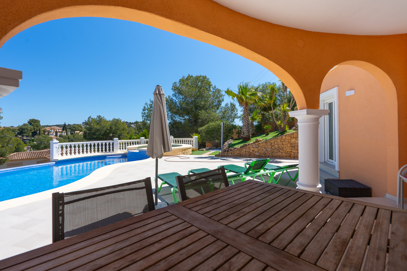 Terraza cubierta con arcos tradicionales que ofrece vistas directas a la piscina privada, zona de solárium y jardín mediterráneo con muros de piedra natural.