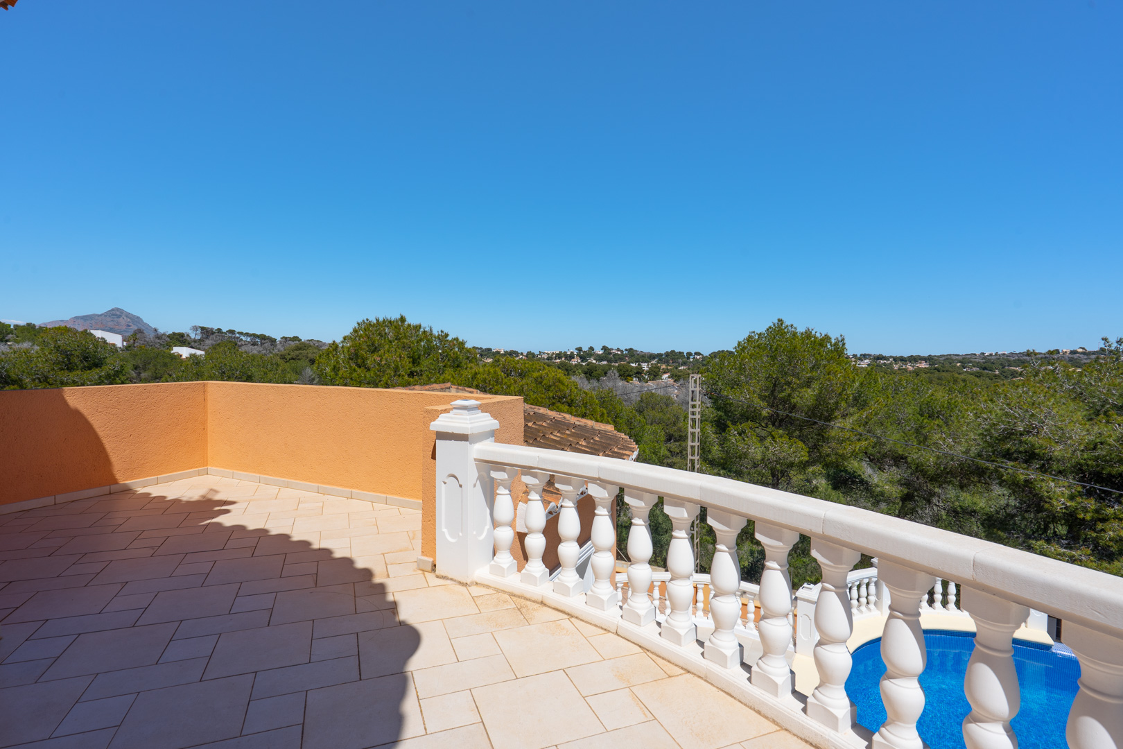 Terraza superior con pavimentos cerámicos y balaustrada clásica blanca, ofreciendo vistas despejadas al entorno natural y a la piscina privada.