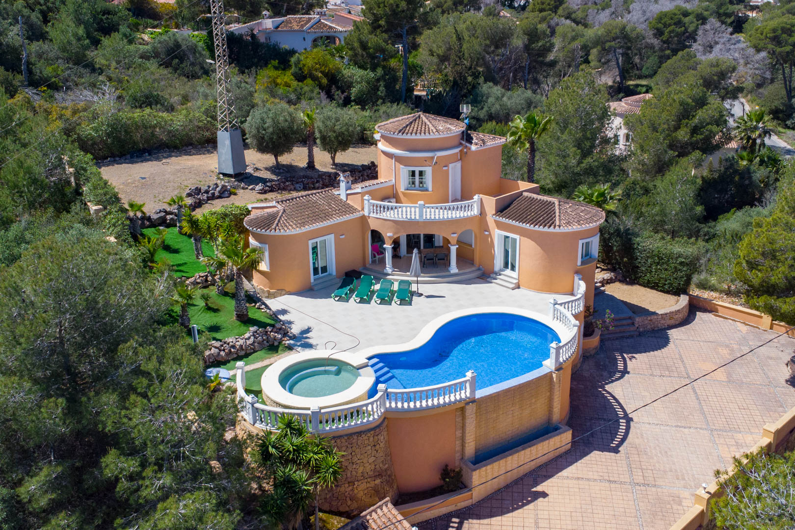 Vista aérea de la villa mediterránea con piscina de forma irregular, jacuzzi integrado y amplia terraza rodeada de vegetación autóctona y pinos.