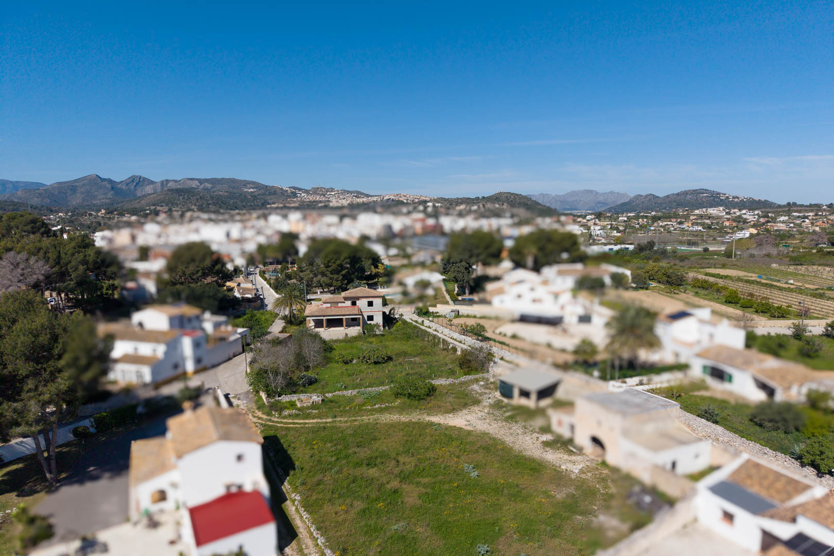 Vista aérea de la parcela de 1800 m² con la estructura de la vivienda principal y construcciones anexas, rodeada de vegetación y con vistas a las montañas.