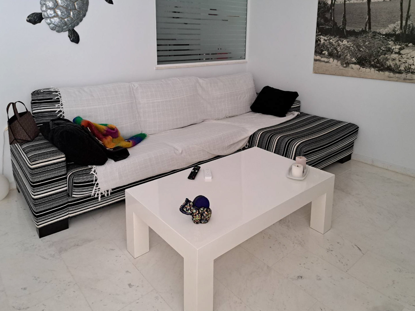 Salón con suelos de mármol, sofá esquinero con tapicería de rayas y una mesa de centro blanca minimalista sobre un pavimento de piedra natural clara.