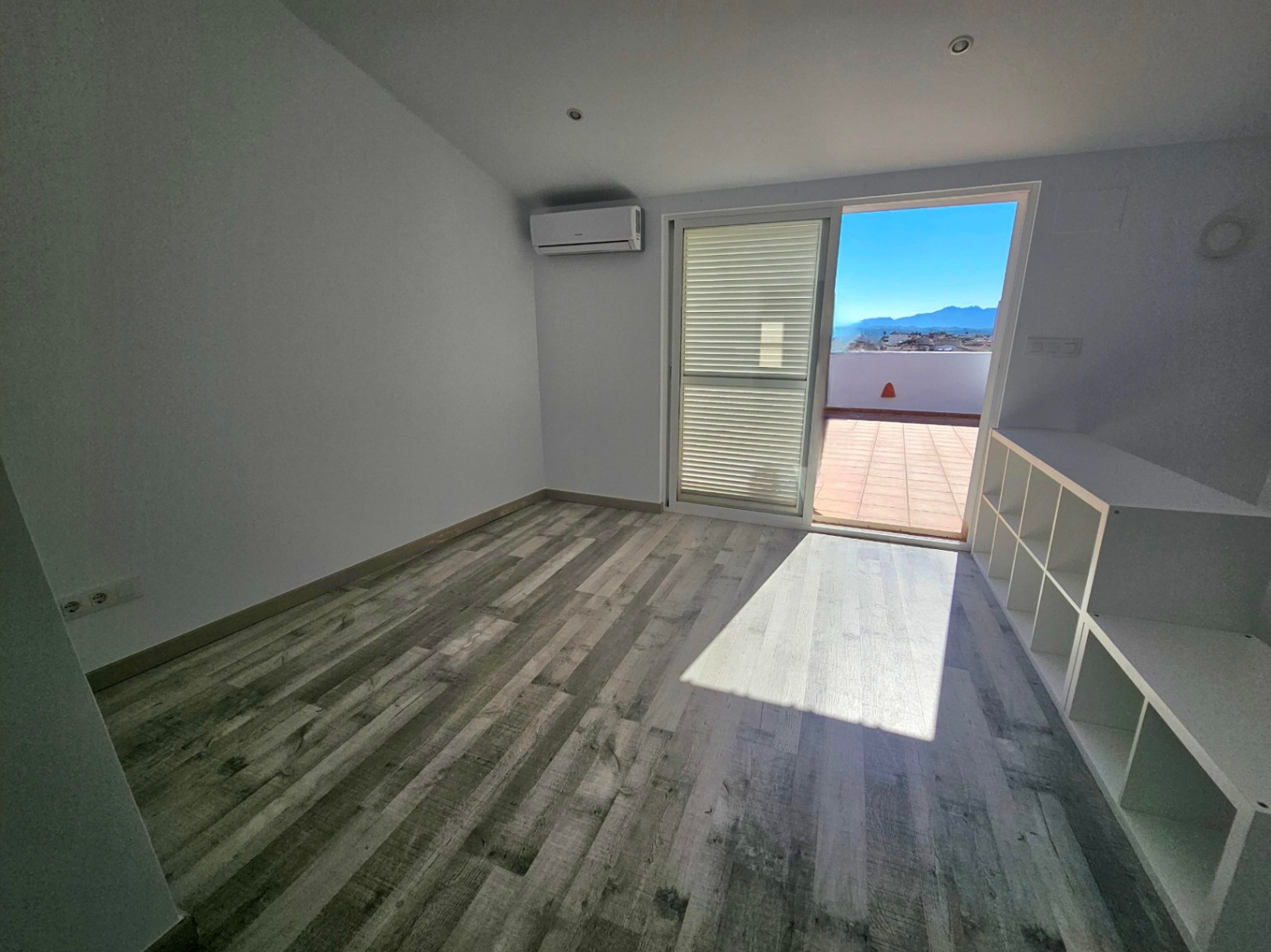 Despacho luminoso con suelos de madera, aire acondicionado y acceso directo a una terraza privada con vistas panorámicas a las montañas.