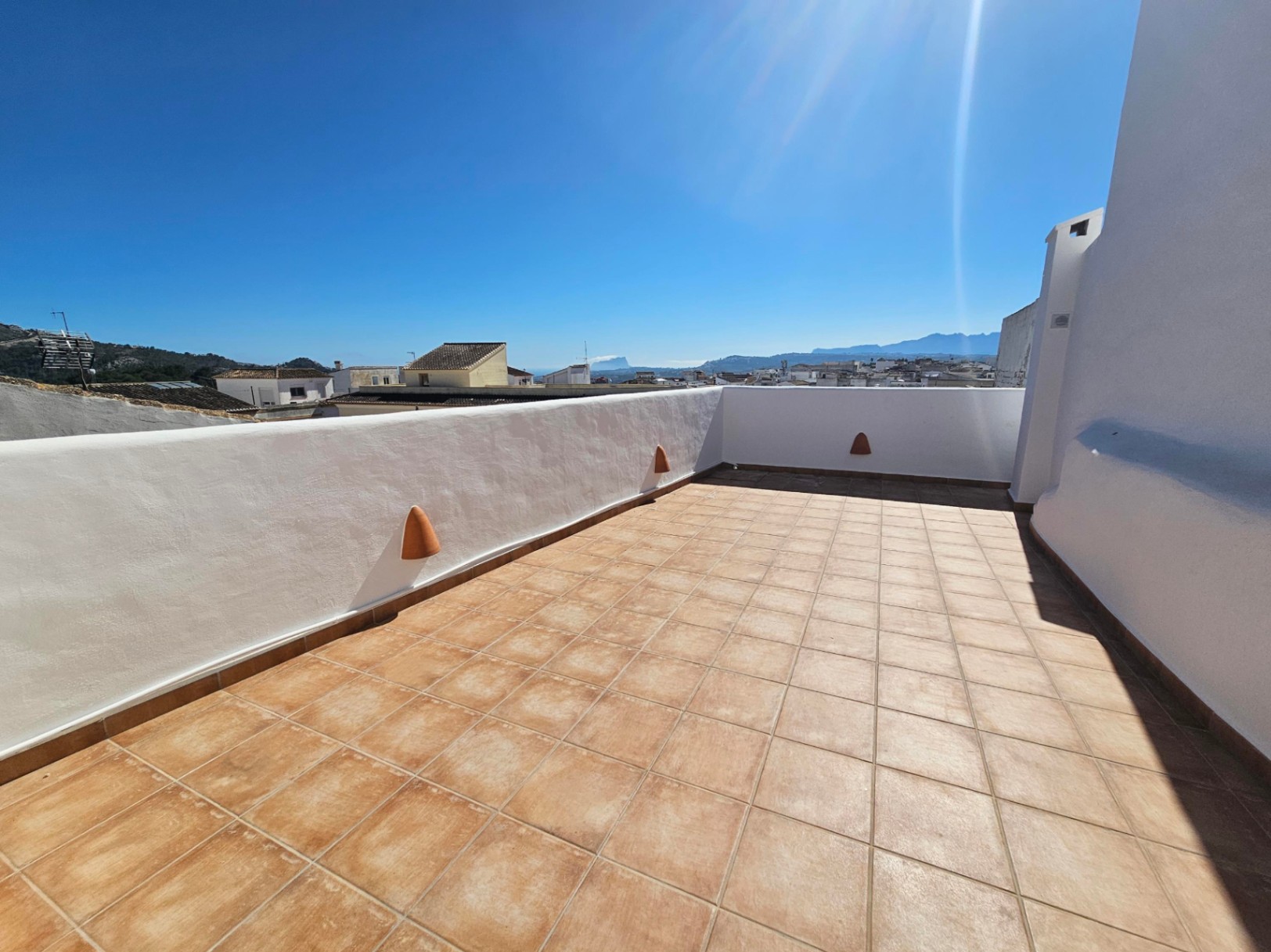 Terraza privada en la planta superior con suelos de gres cerámico, muros blancos y vistas panorámicas al pueblo, las montañas y el Peñón de Ifach al fondo.