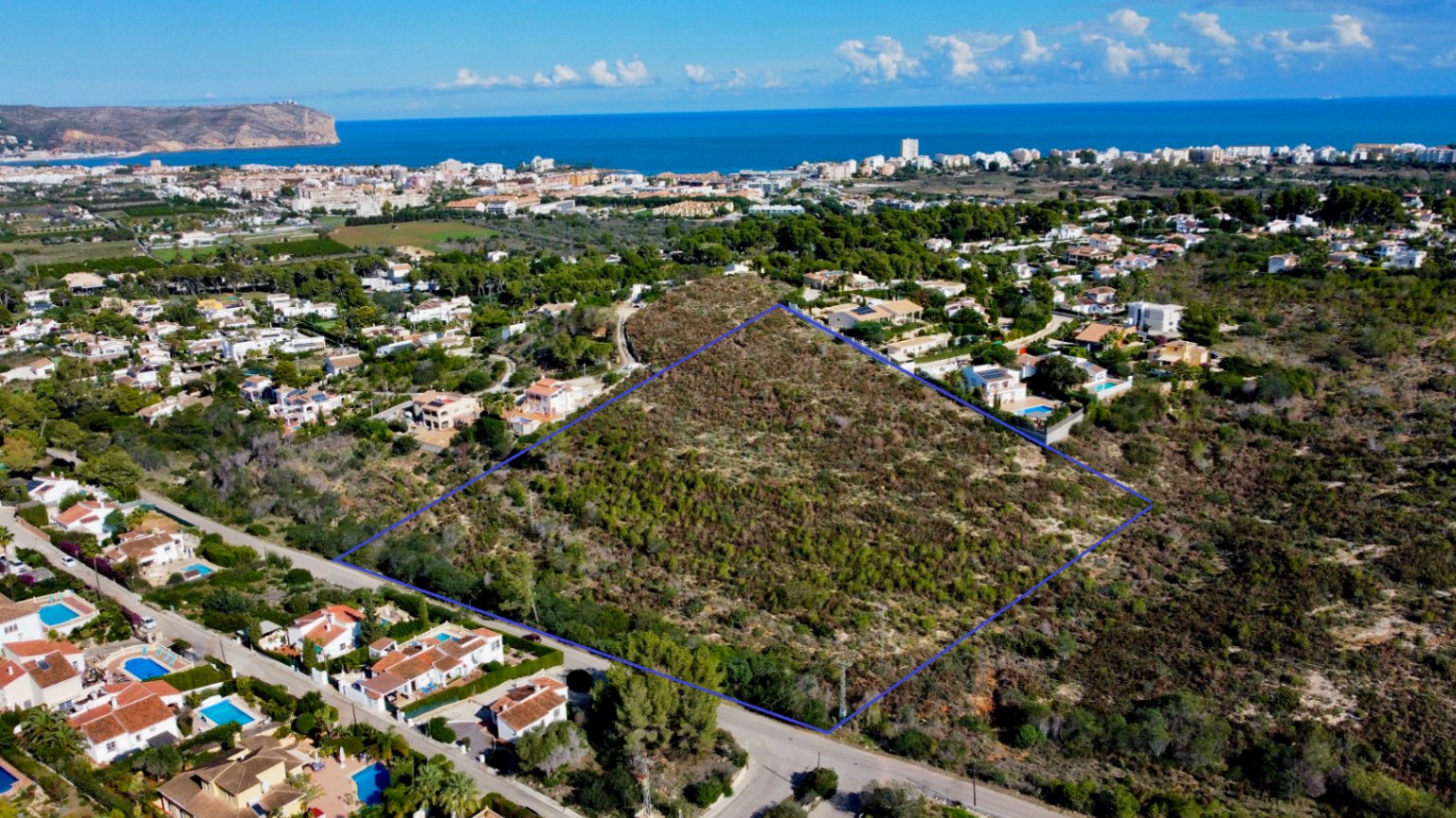 Vista aérea de la parcela de 17.272 m² en Jávea, delimitada en azul, rodeada de zonas residenciales con vistas al mar Mediterráneo y al Cabo de San Antonio.
