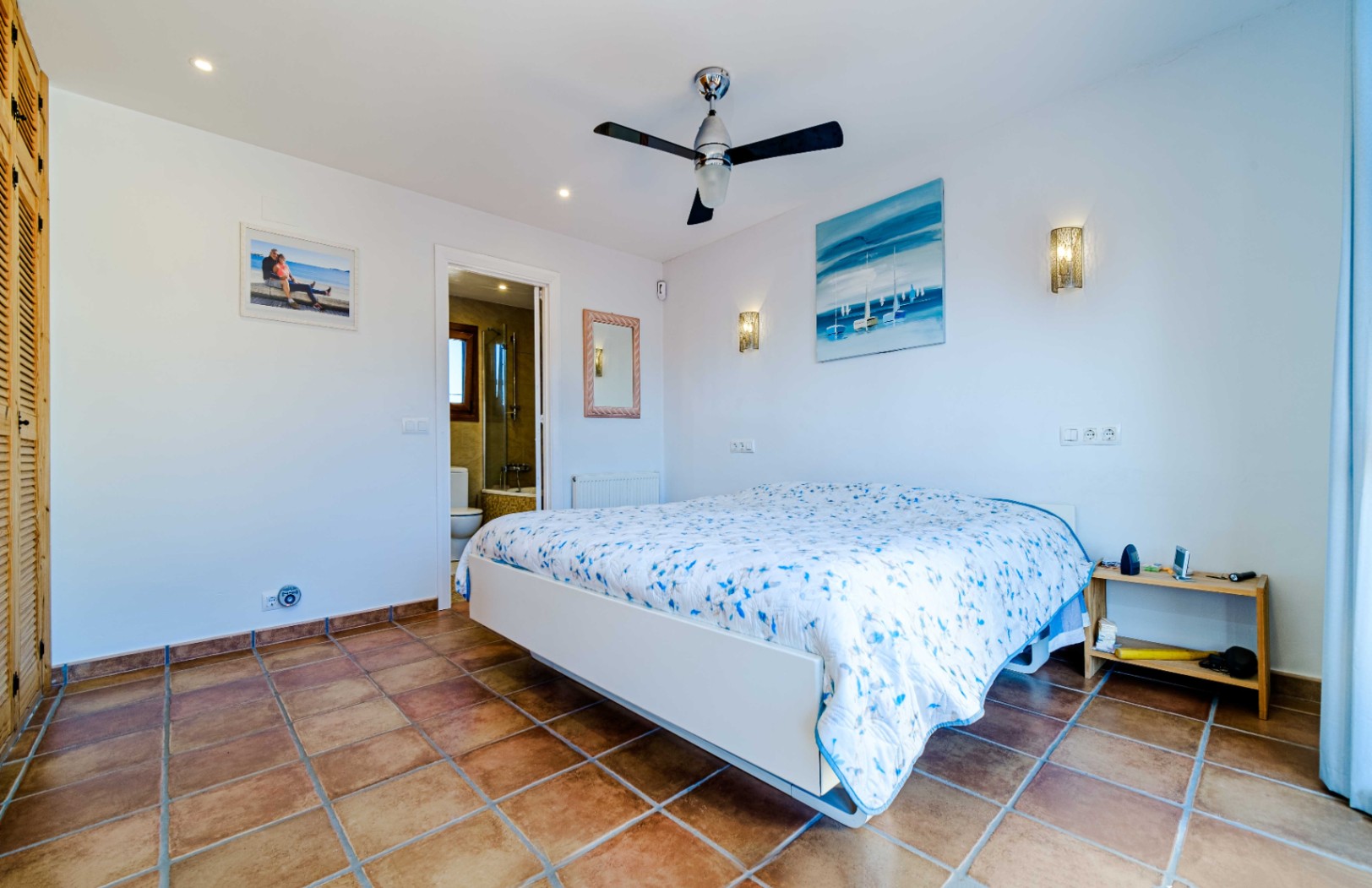 Dormitorio luminoso con suelo de terracota, ventilador de techo y baño en suite. Incluye armarios empotrados de madera y una distribución funcional.
