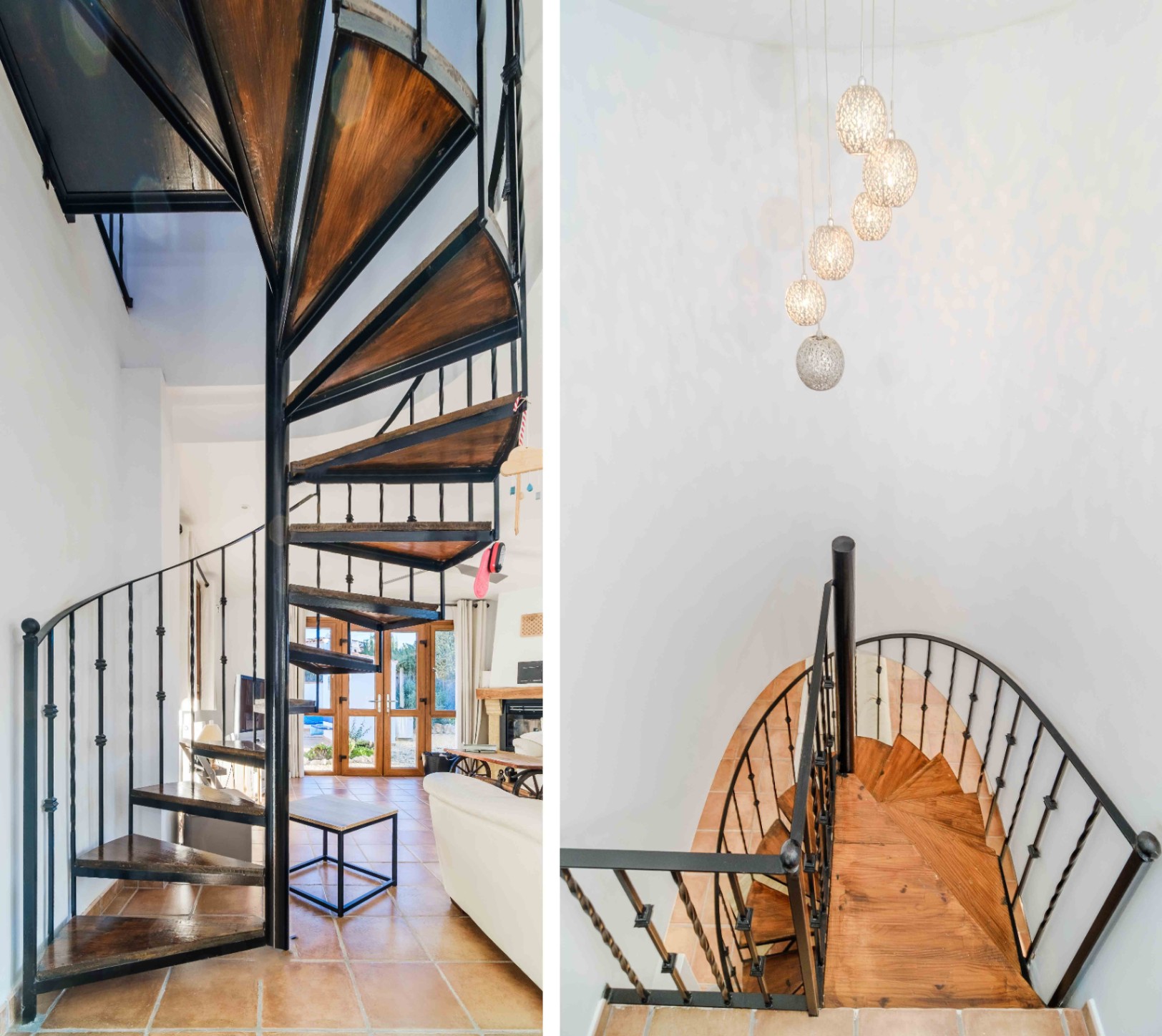 Escalera de caracol con peldaños de madera y barandilla de hierro forjado, iluminada por una moderna lámpara de esferas sobre suelos de terracota.