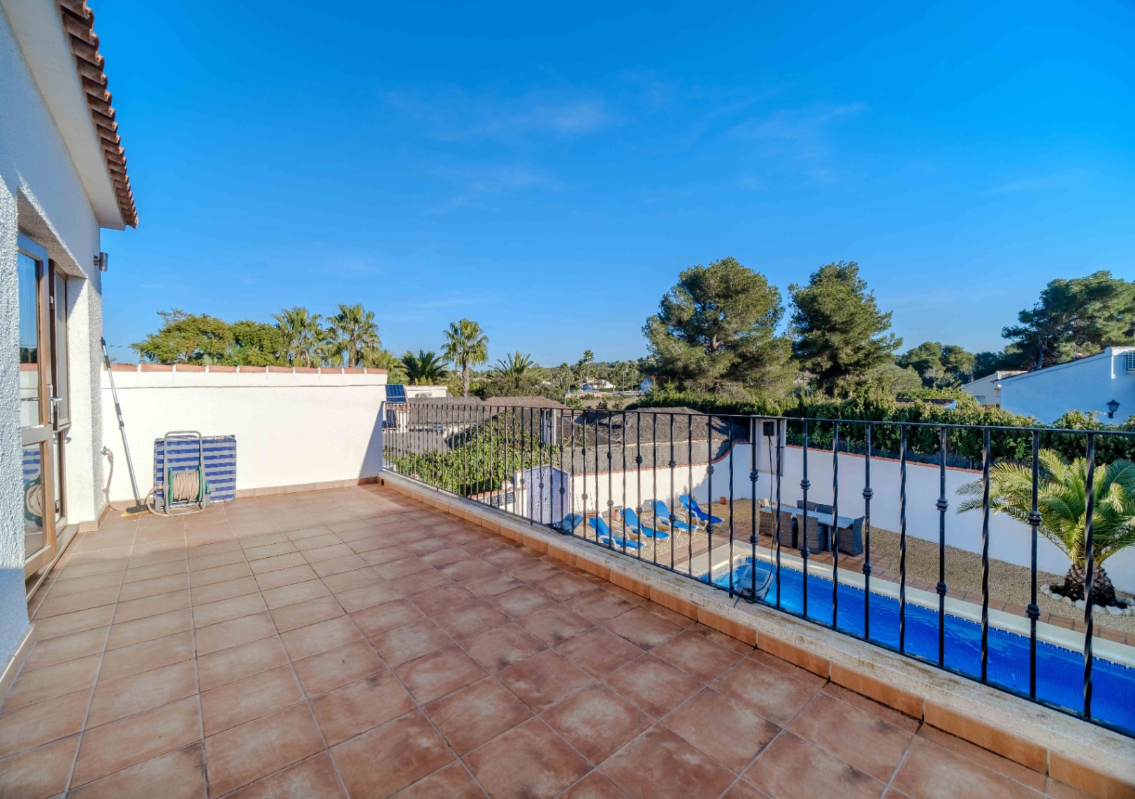 Terraza superior con suelo de gres cerámico y barandilla de forja negra, con vistas despejadas a la piscina privada y al entorno arbolado de Costa Nova.